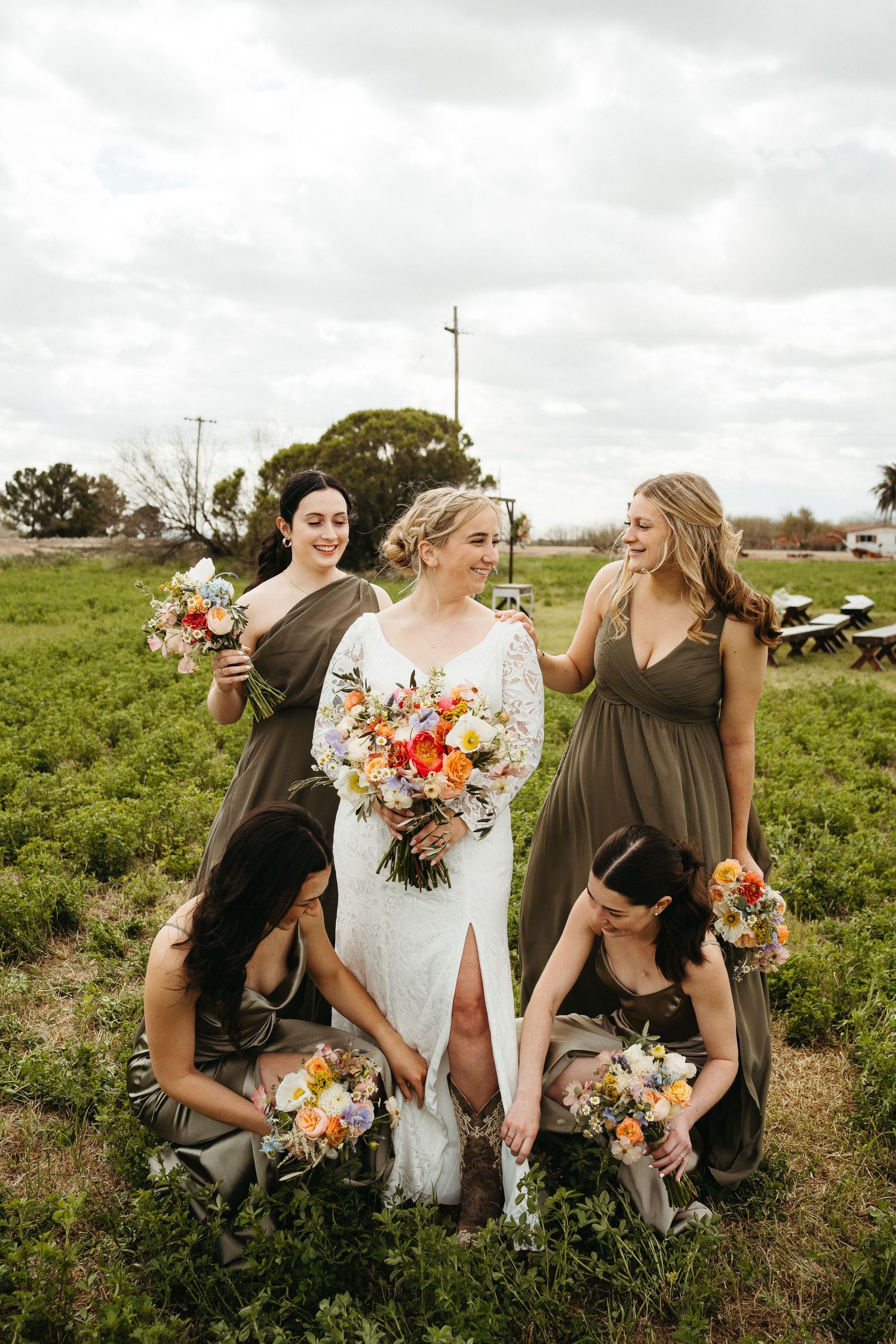 Wedding party poses together in an outdoor field with colorful bouquets and olive green dresses.