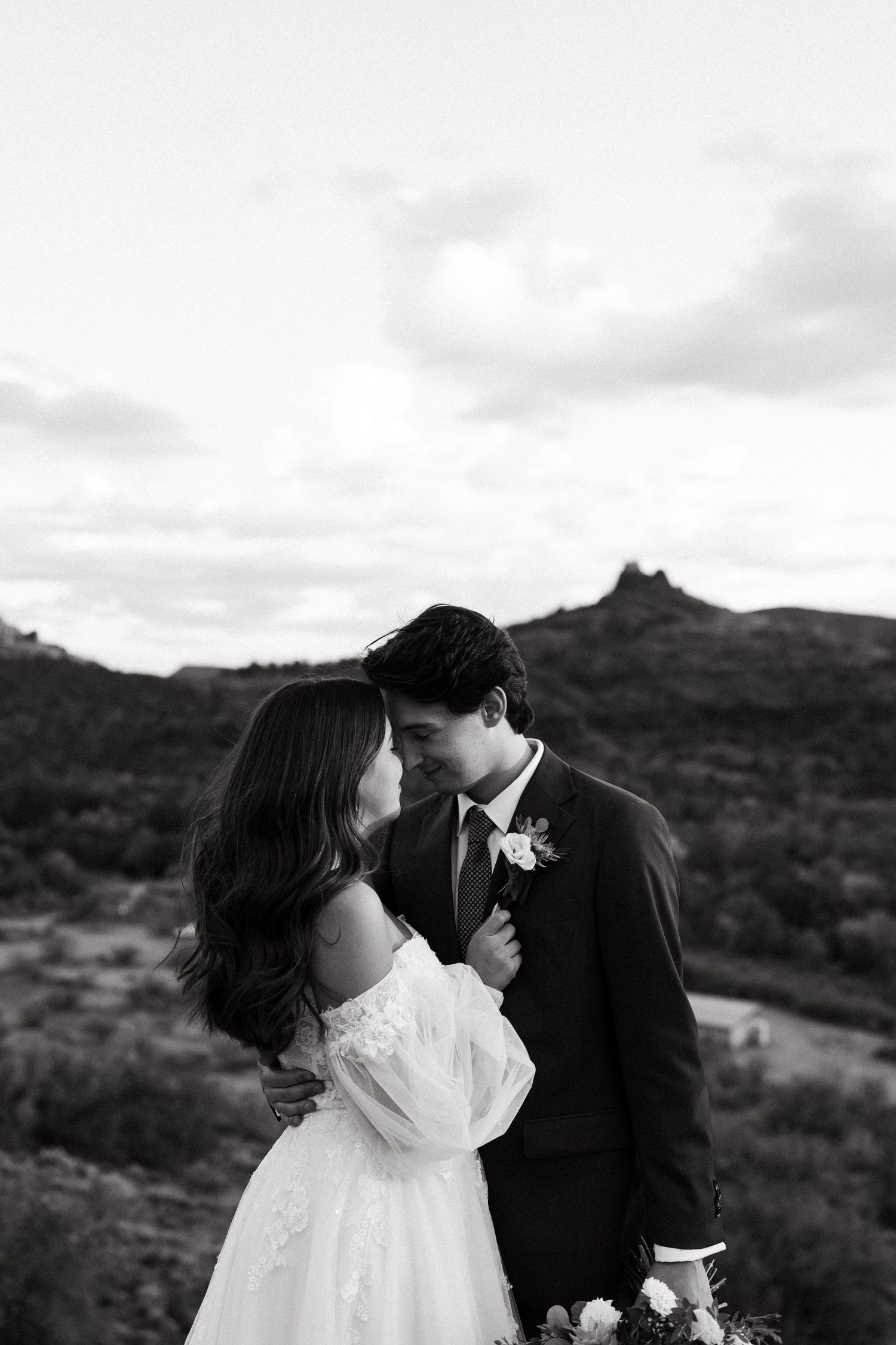 A romantic couple shares an intimate moment against a desert mountain landscape at sunset.