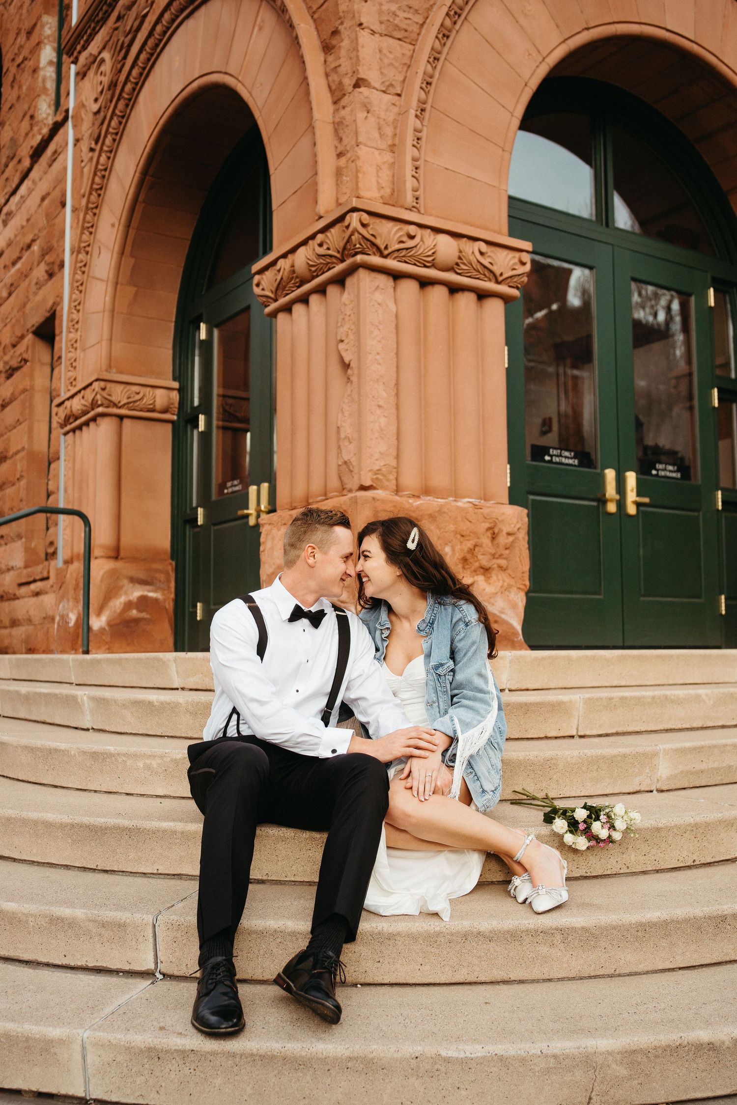 A couple sits intimately on stone steps of a historic building with ornate architecture.