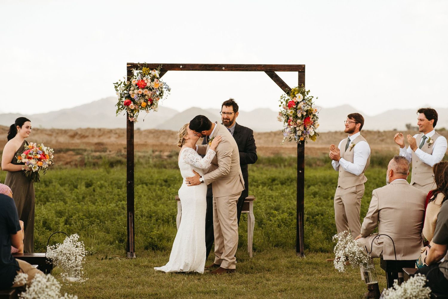 Wedding celebration under wooden arch with desert landscape backdrop and seated guests.