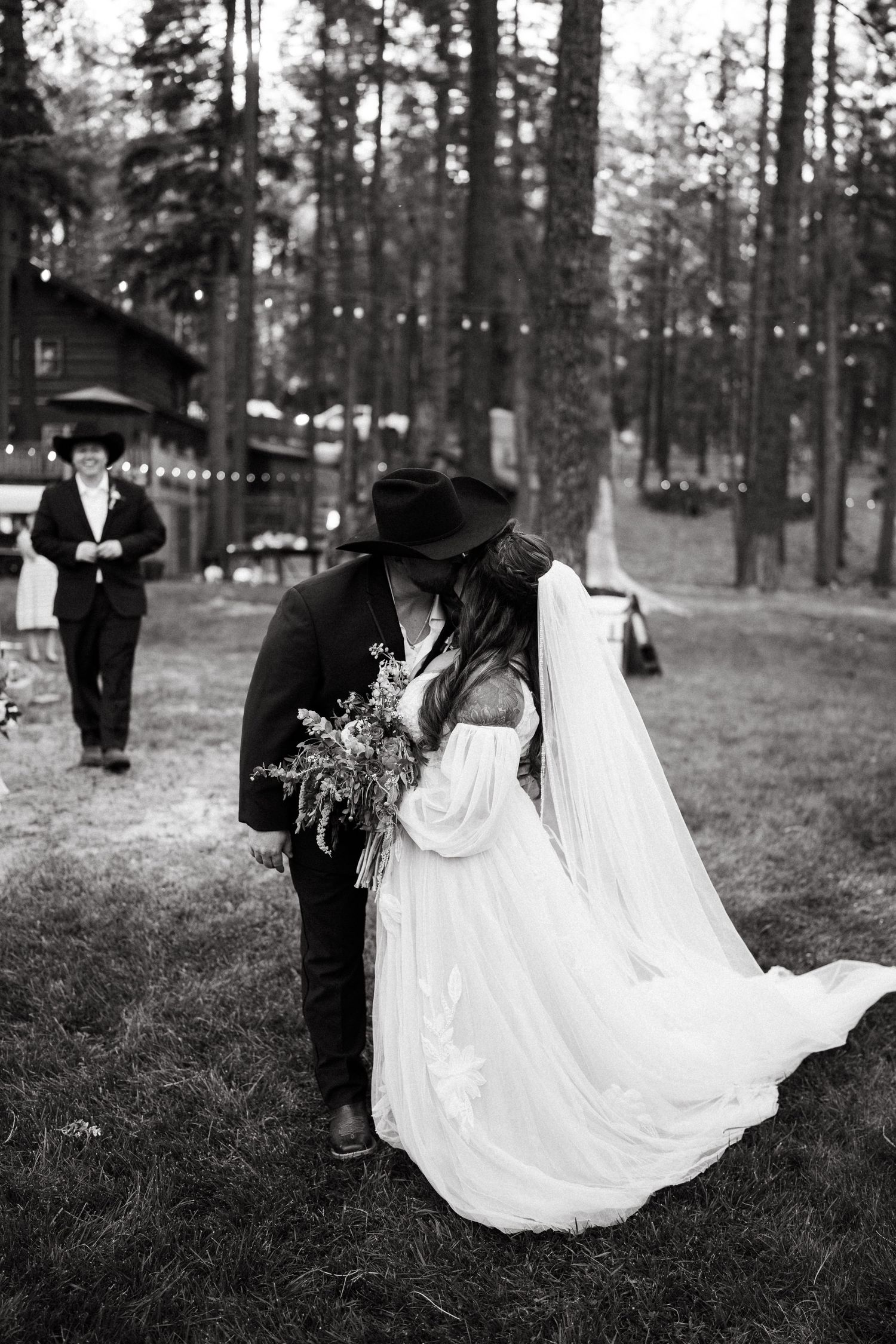 Intimate black and white wedding moment between couple surrounded by pine trees.