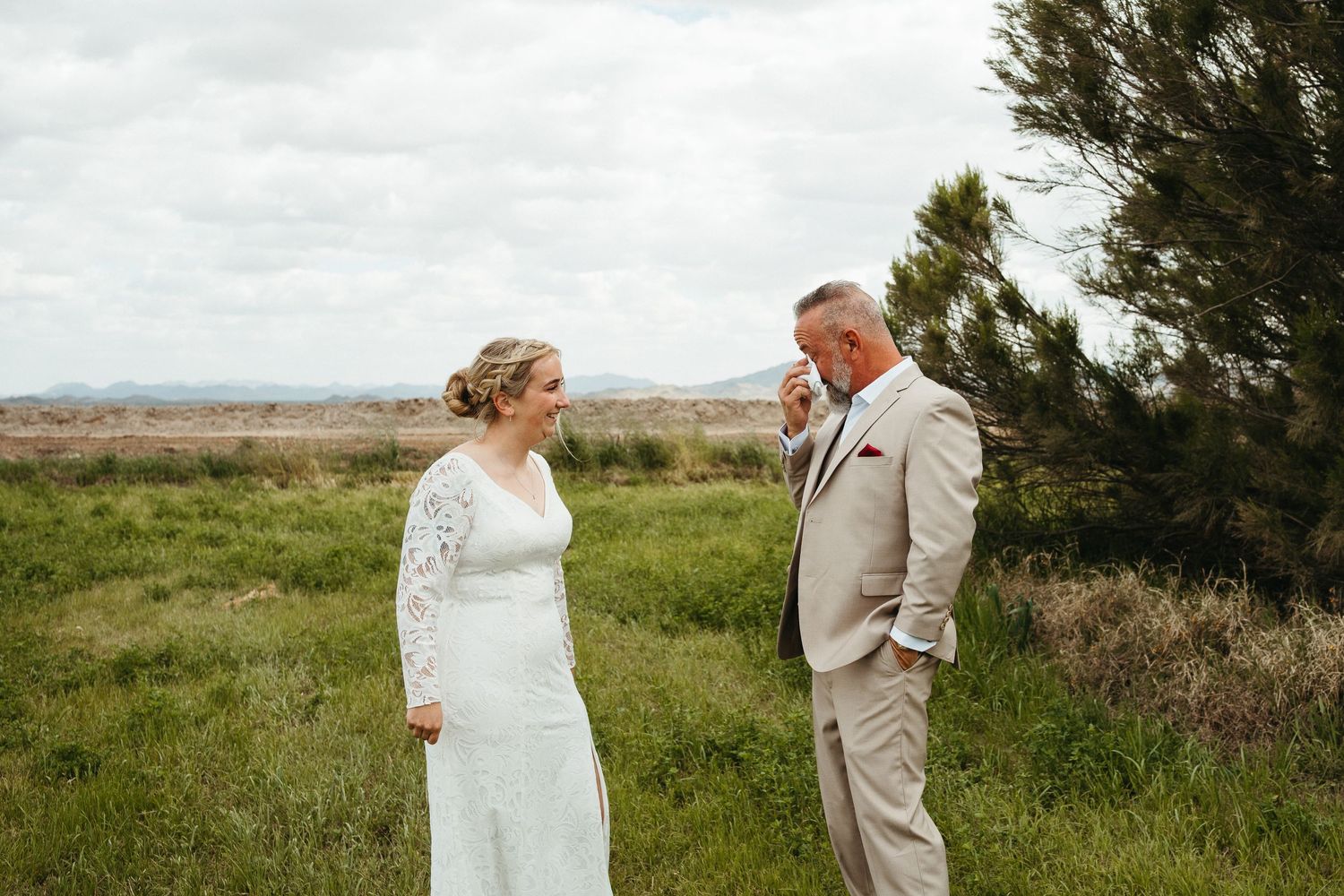 A candid wedding moment captured between a couple wearing white and beige on a hilltop.