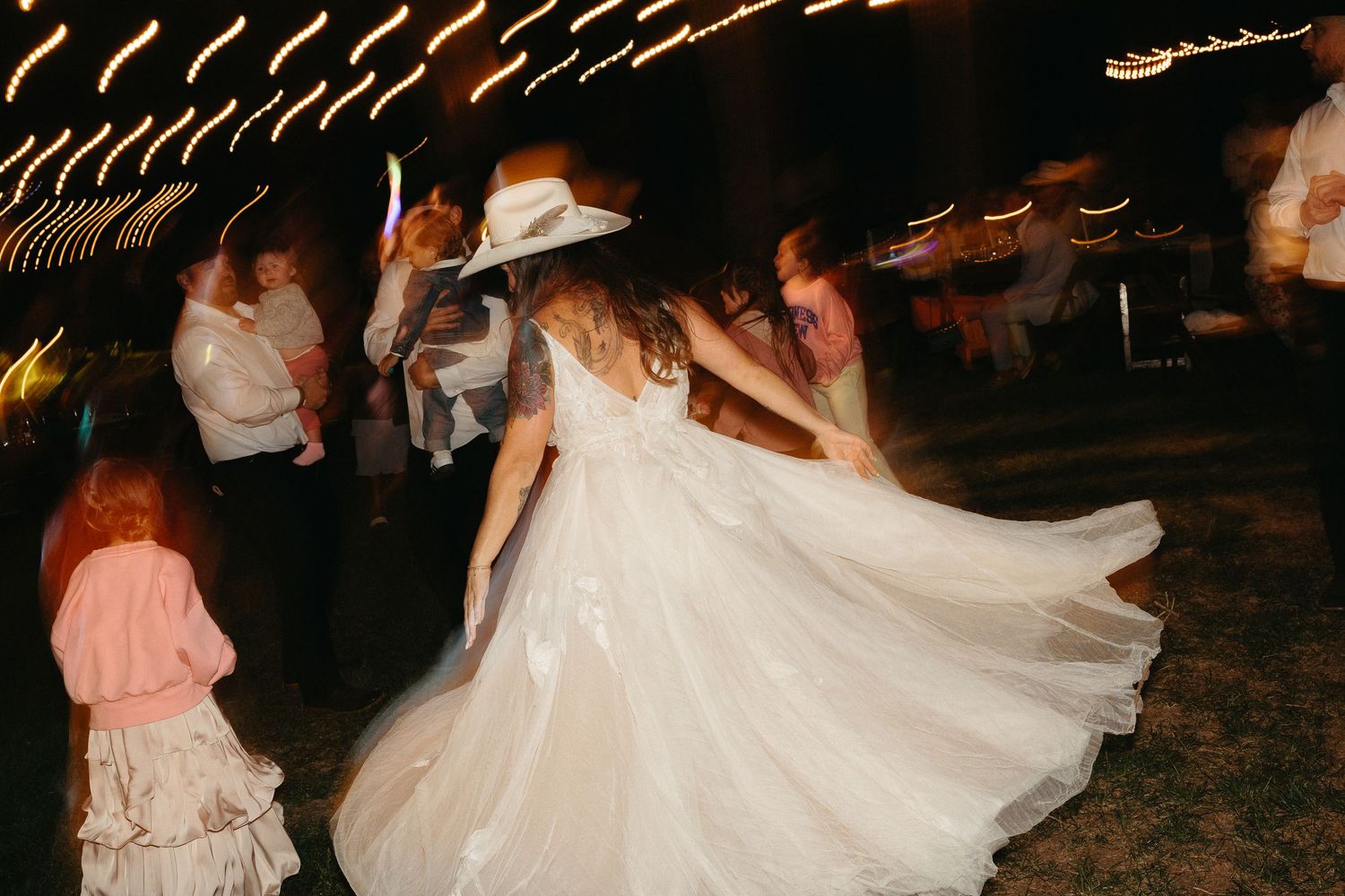 A bride in a flowing white wedding dress twirls gracefully on a dance floor at night.