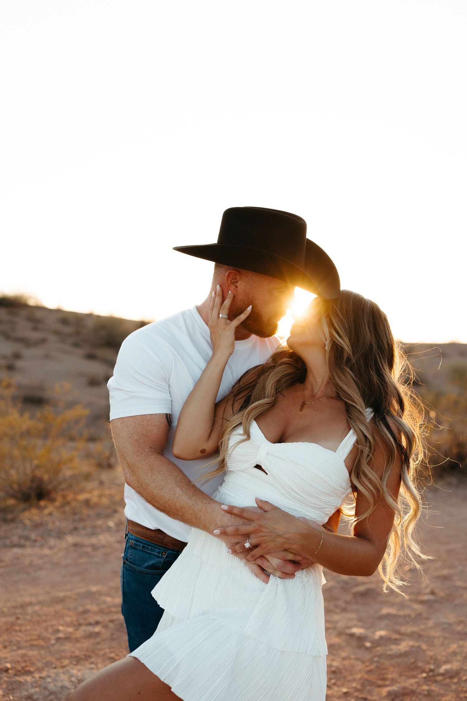 A romantic desert photoshoot with a couple in western wear embracing during golden hour.