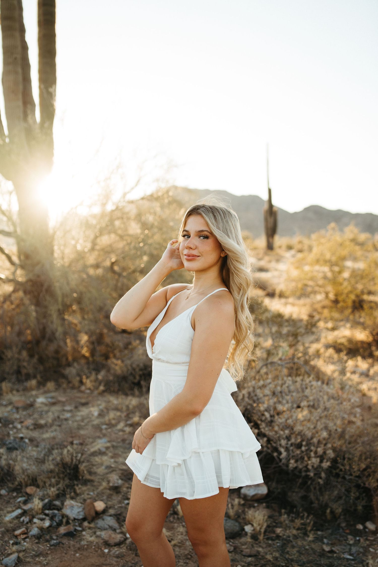 Person in white summer dress poses in front of saguaro cactus during desert sunset.