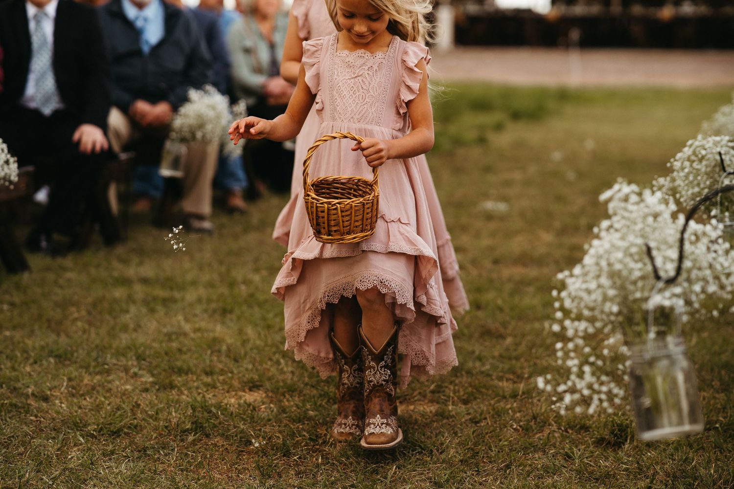 Young flower girl in pink dress carries basket down aisle lined with baby's breath flowers.
