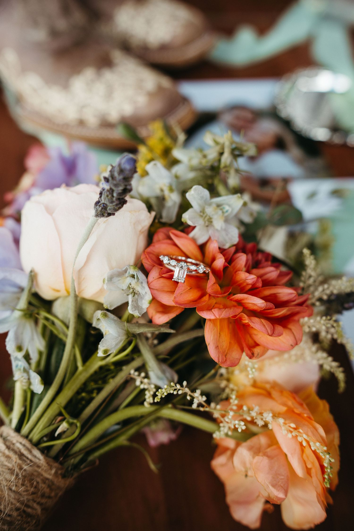 Colorful bridal bouquet with coral and white flowers displayed with engagement ring.