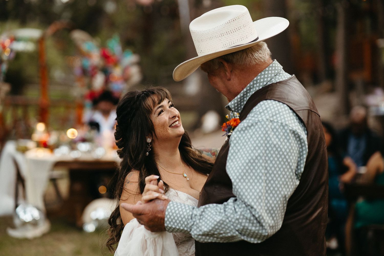 A couple in western attire dances together outdoors at a country-themed celebration.
