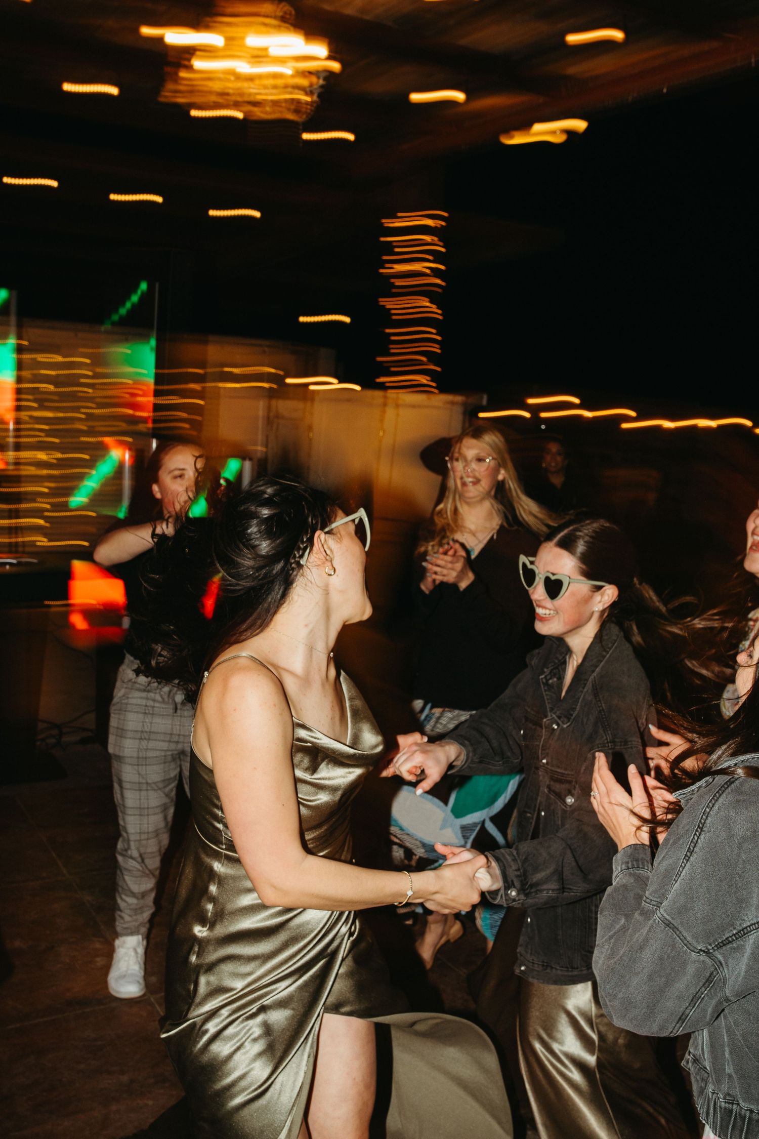 Party guests dancing and enjoying themselves at a dimly lit reception with colorful lighting.