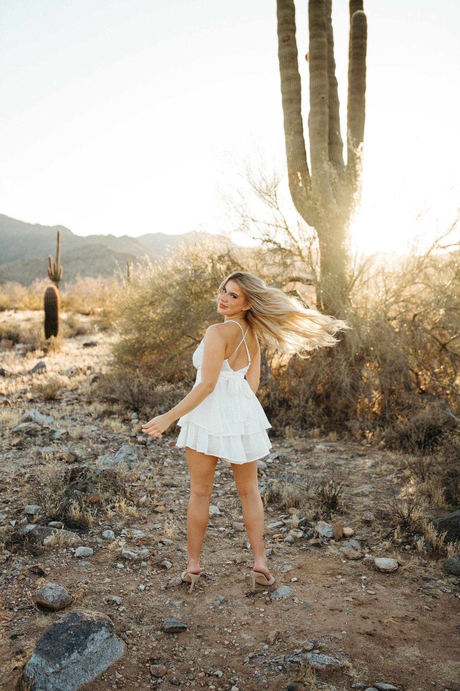 Figure in white dress twirls in front of saguaro cactus during desert sunset.