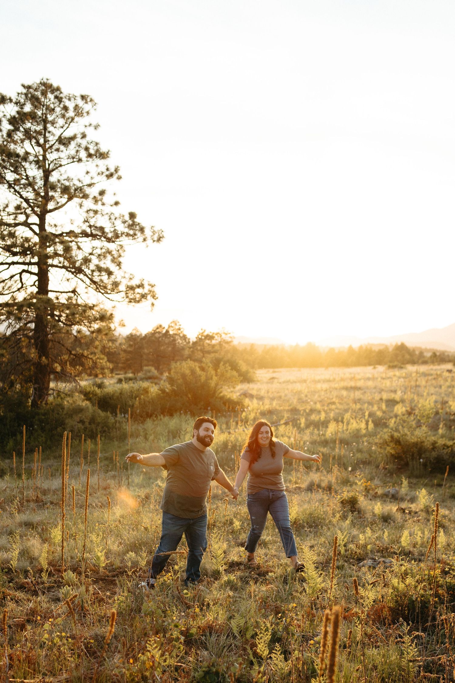 Couple holding hands and dancing in a sunlit field during golden hour.
