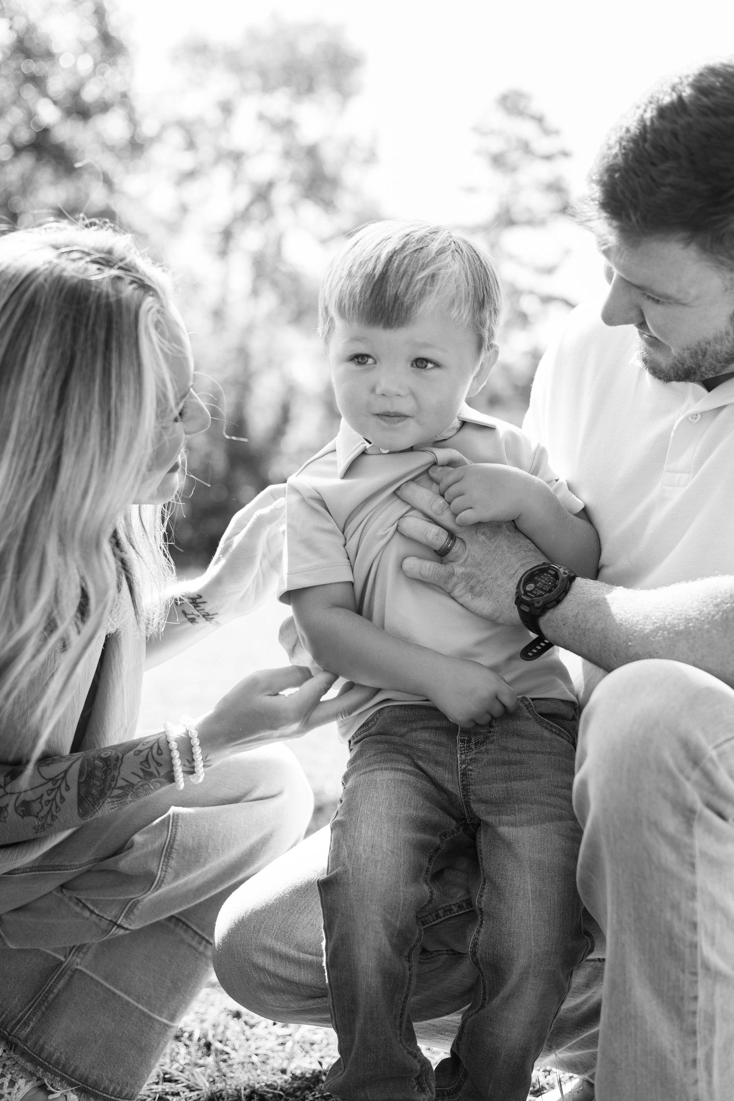 Black and white photo of parents crouching with their toddler son outdoors in a park setting.