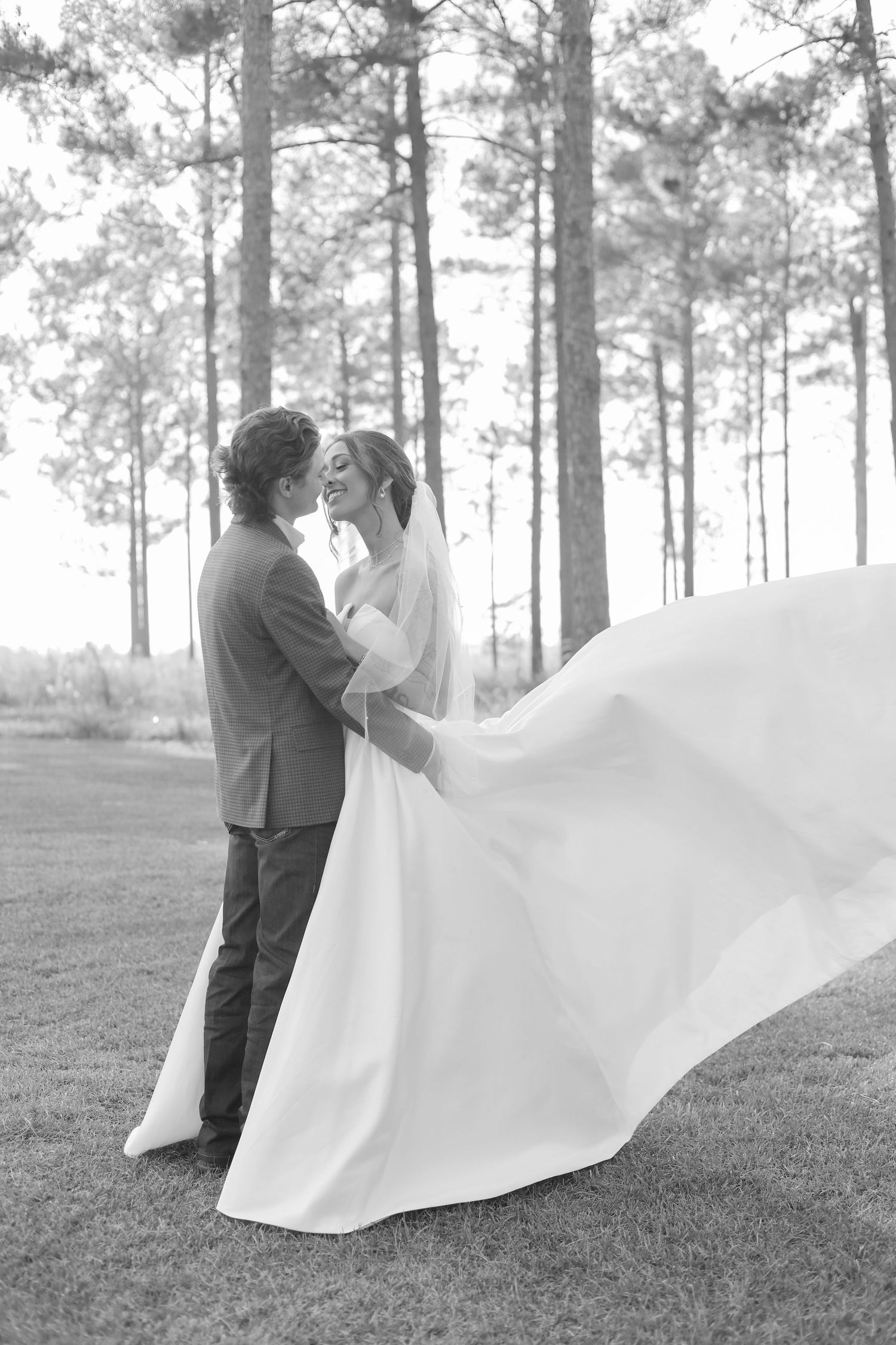A dramatic black and white wedding photo with flowing dress fabric in a forest setting.