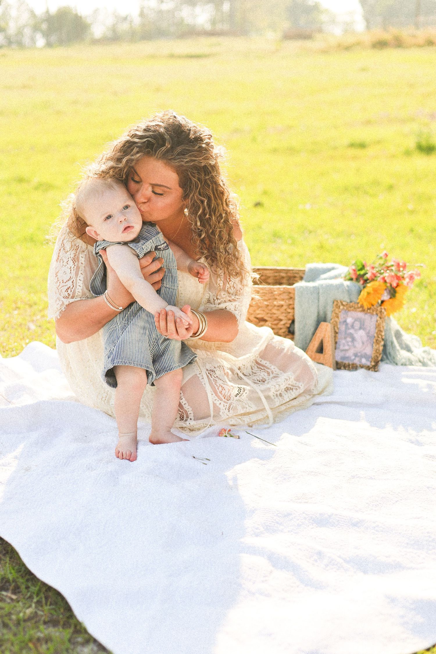 Mother and child portrait session on white blanket in sunny field.