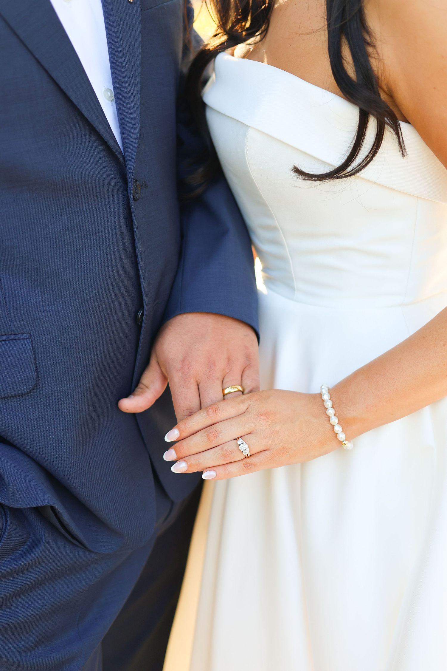 Close-up details of wedding rings and formal attire in navy blue and white.