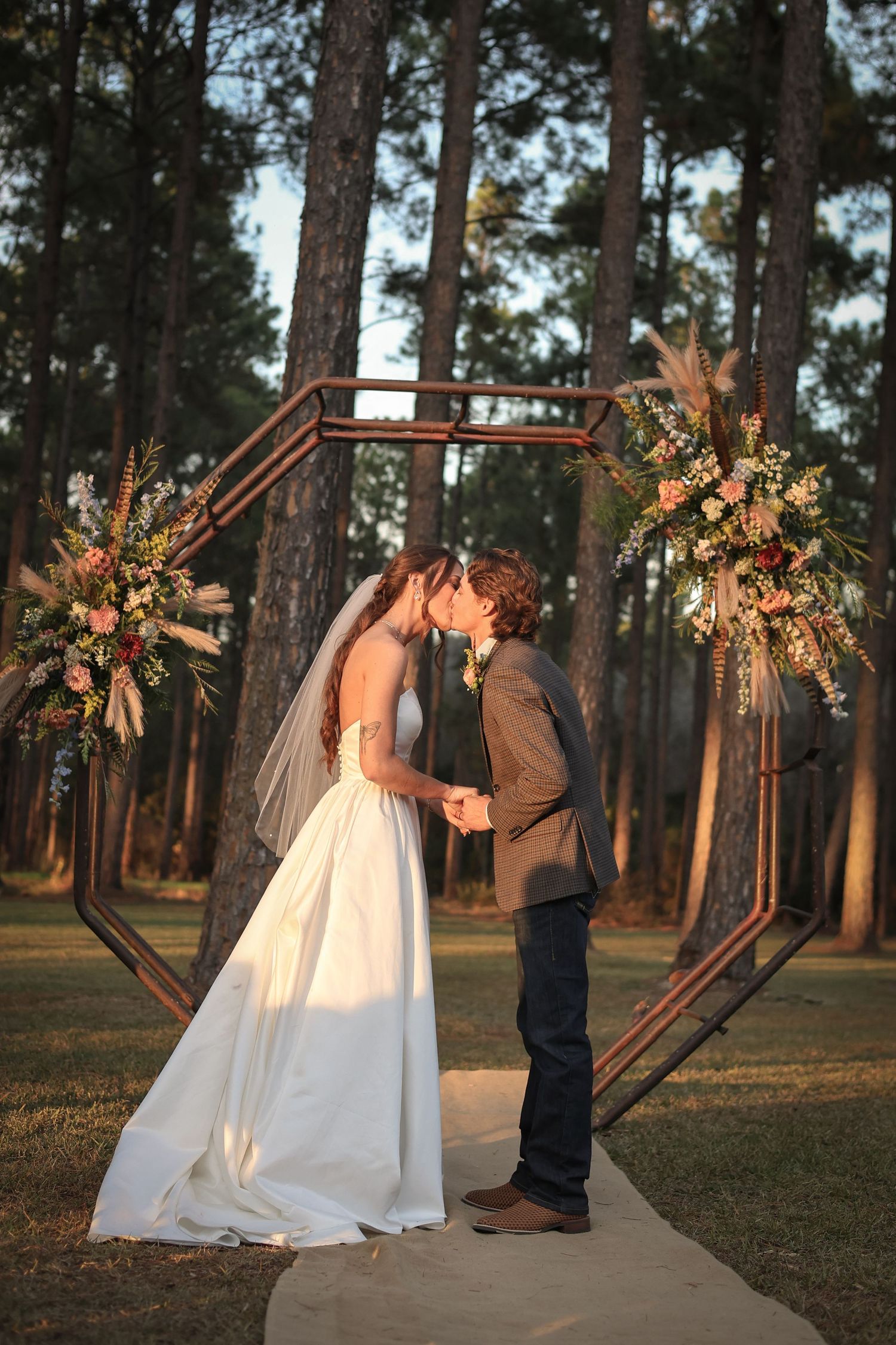 Sunset wedding ceremony with decorative wooden hexagon arch adorned with floral arrangements.