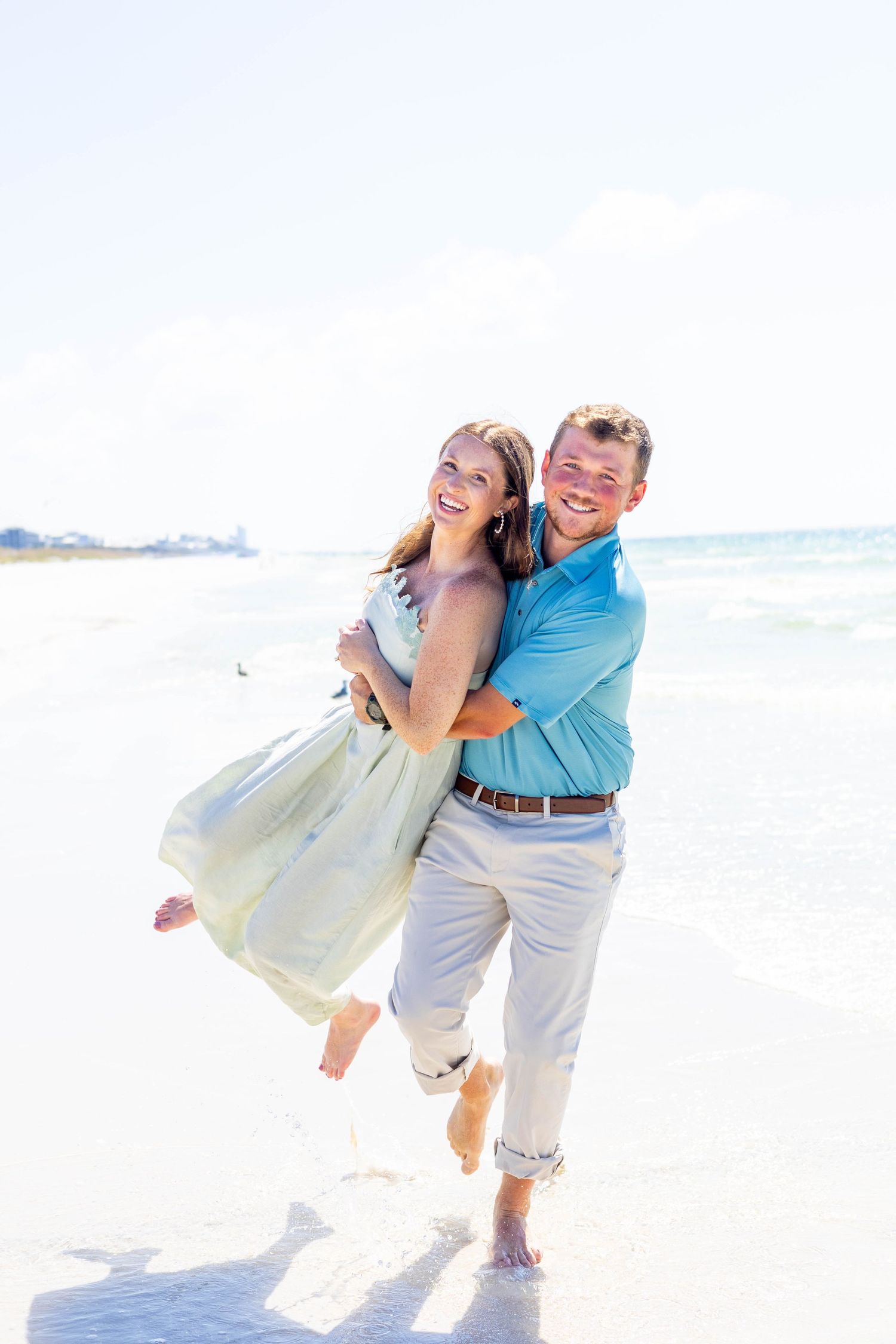 Playful couple laughing and dancing together on a white sandy beach.