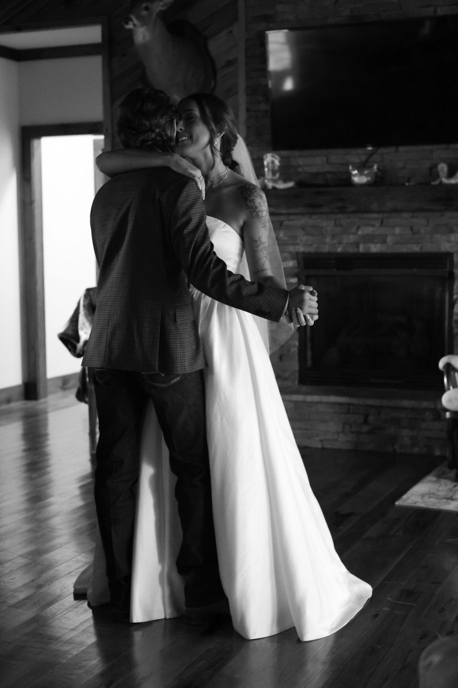 Black and white photo of a bride and groom sharing their first dance near a stone fireplace.