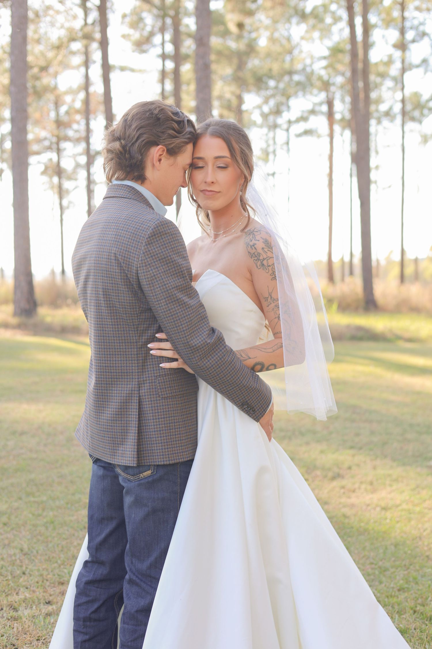 A tender embrace captured in soft lighting among tall pine trees during a wedding.