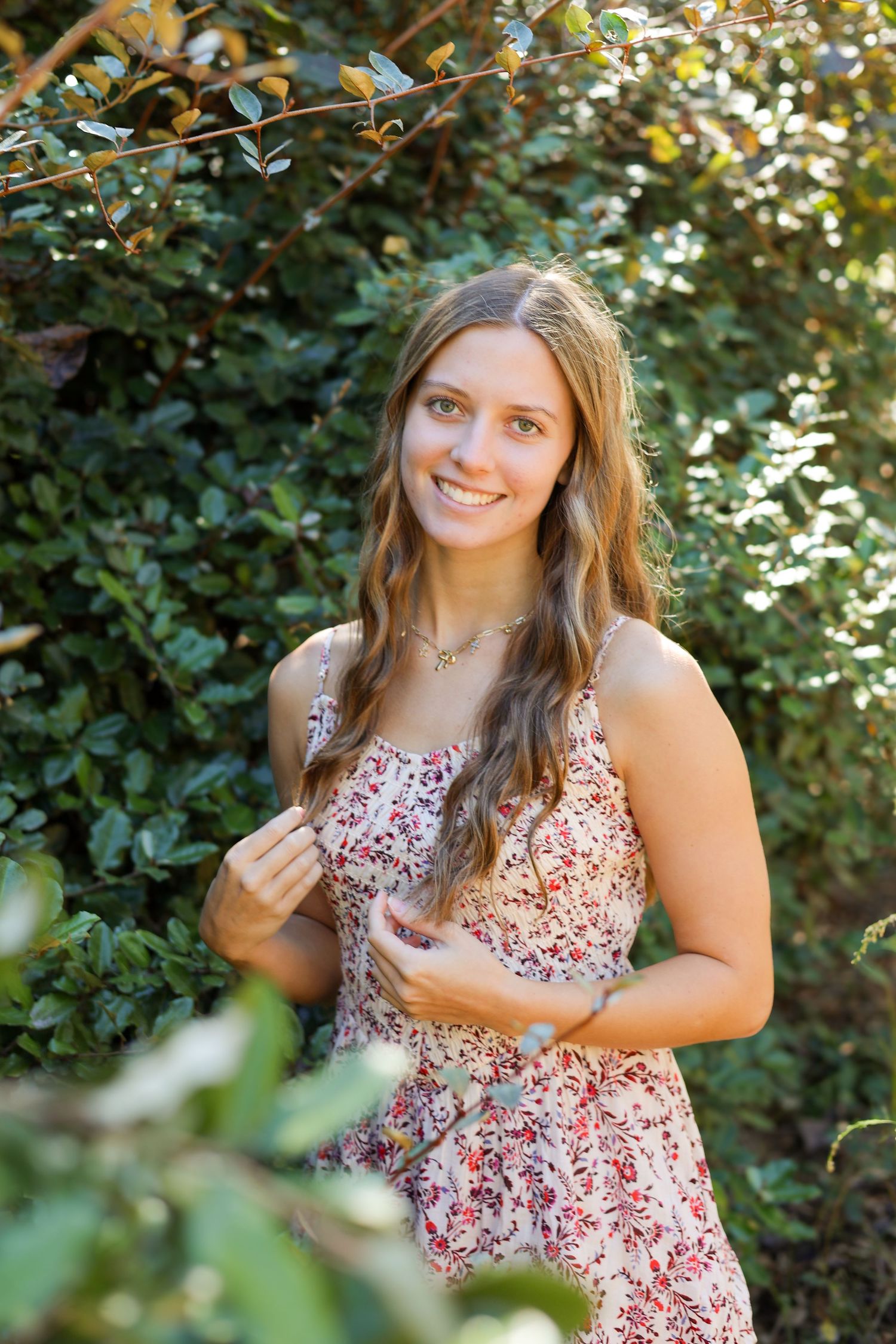 A woman in a floral dress poses outdoors against lush green foliage.
