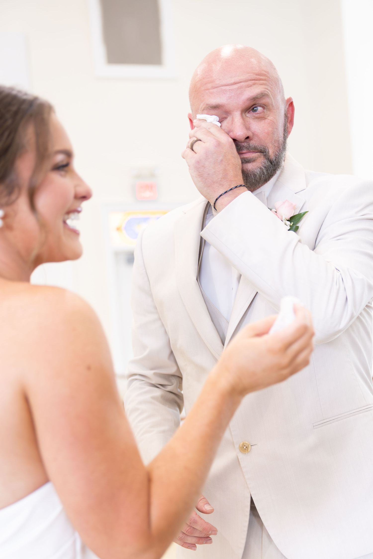 Emotional groom wiping tears while bride laughs during wedding first look moment.