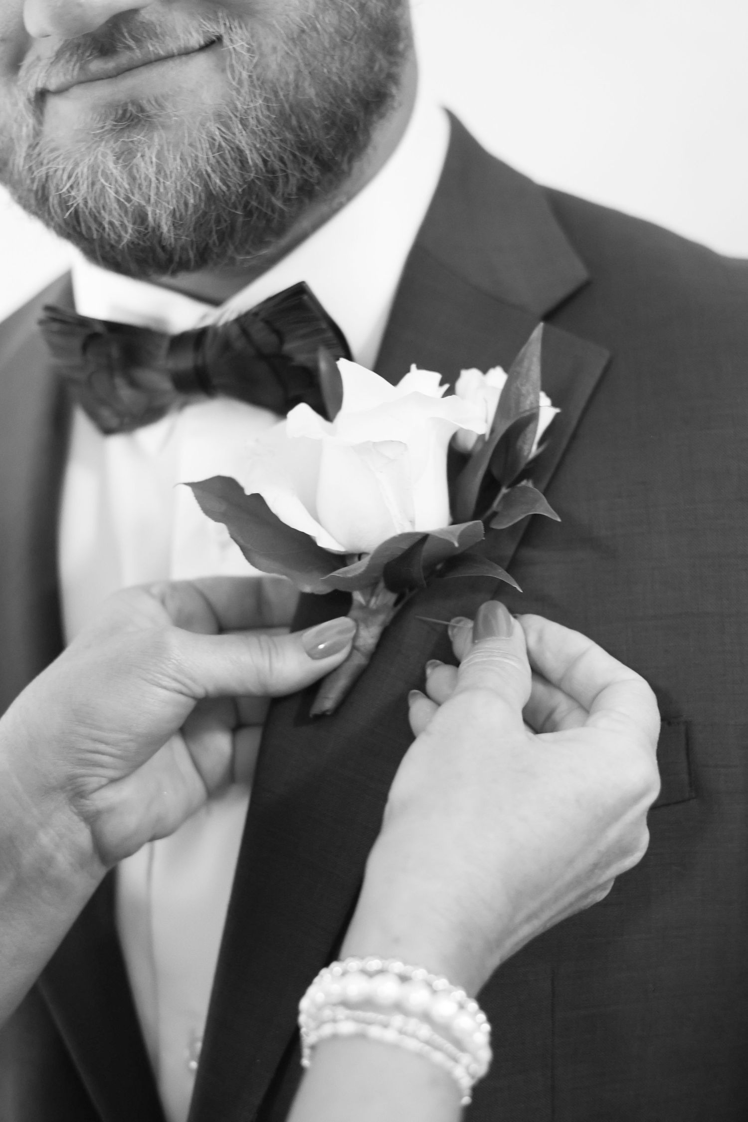 Black and white photo of a bearded groom in a tuxedo having a white rose boutonniere pinned to his lapel.