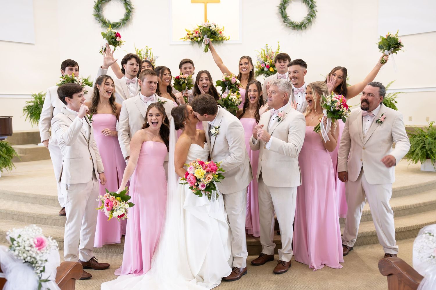 Wedding party in pink dresses and white suits celebrating with bride and groom inside a church.