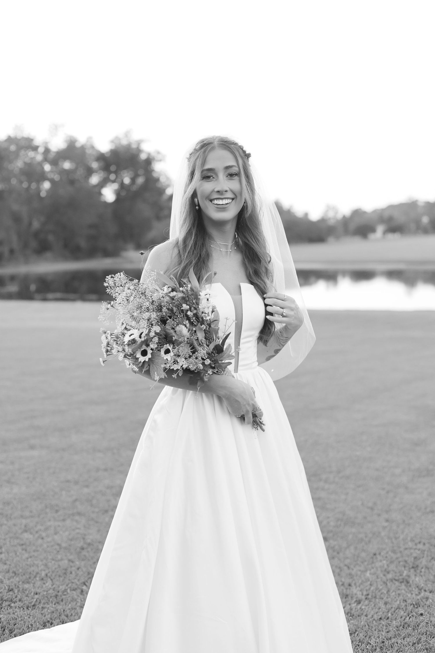 Bride in white dress holds wildflower bouquet while posing in outdoor field setting.