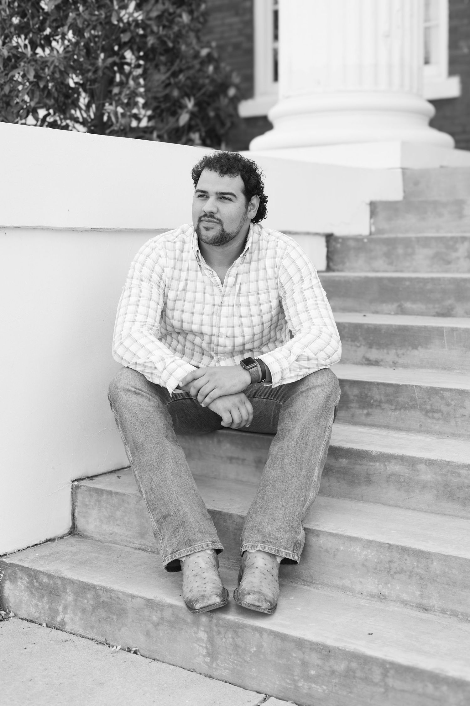 Casual portrait of person sitting on white steps in plaid shirt and jeans.