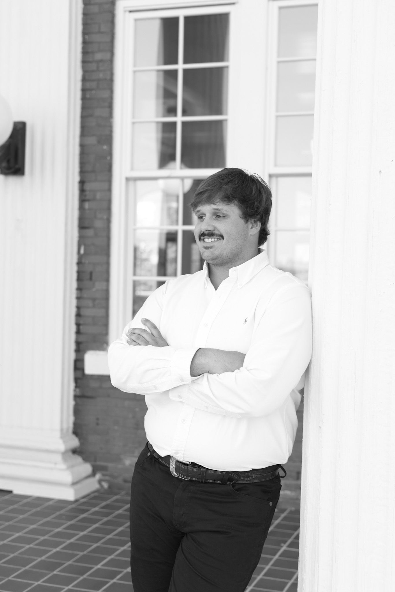 Graduate in academic regalia posing by white columns in black and white photo.