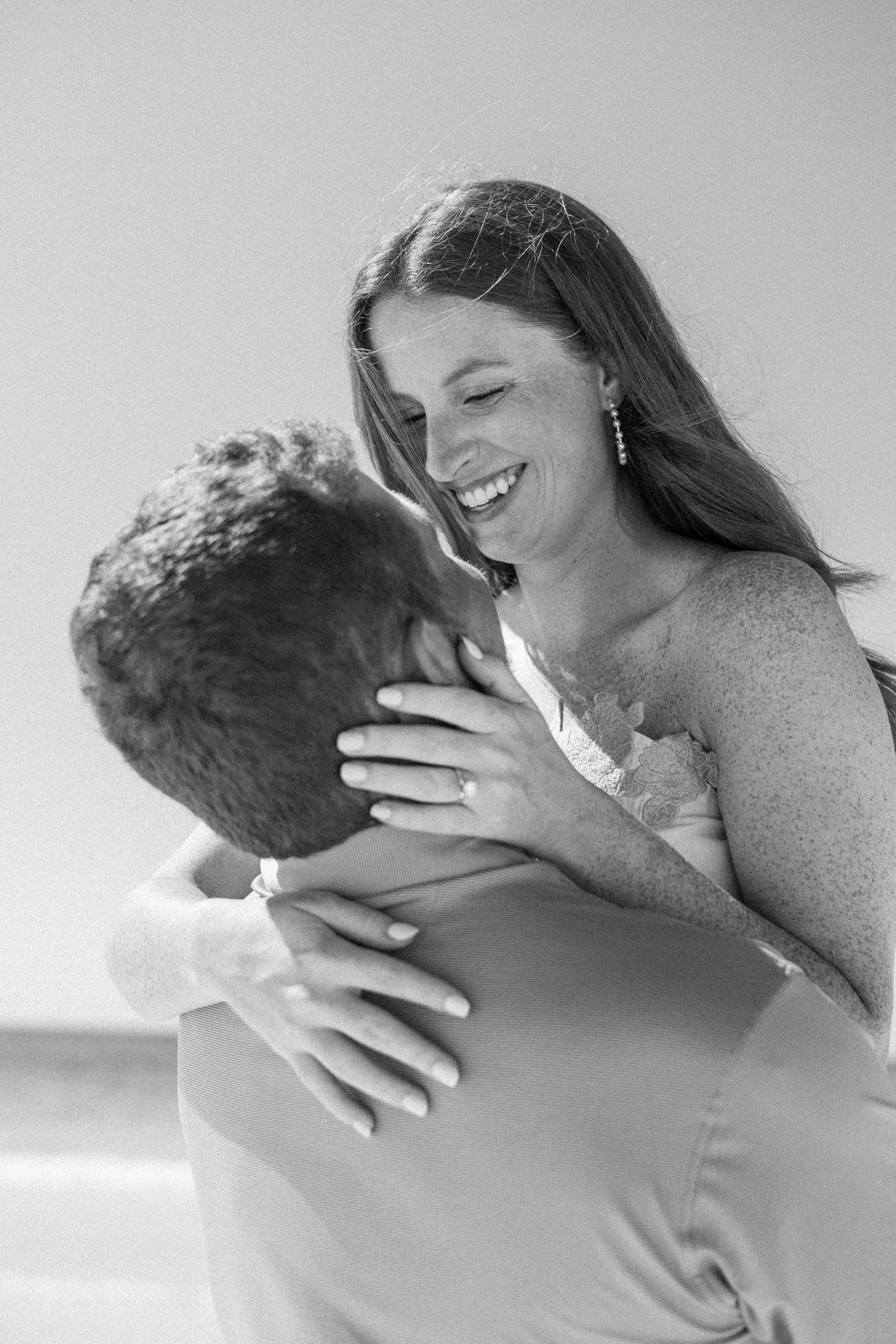 Joyful bride laughing as groom lifts her during a romantic black and white beach engagement photo session.