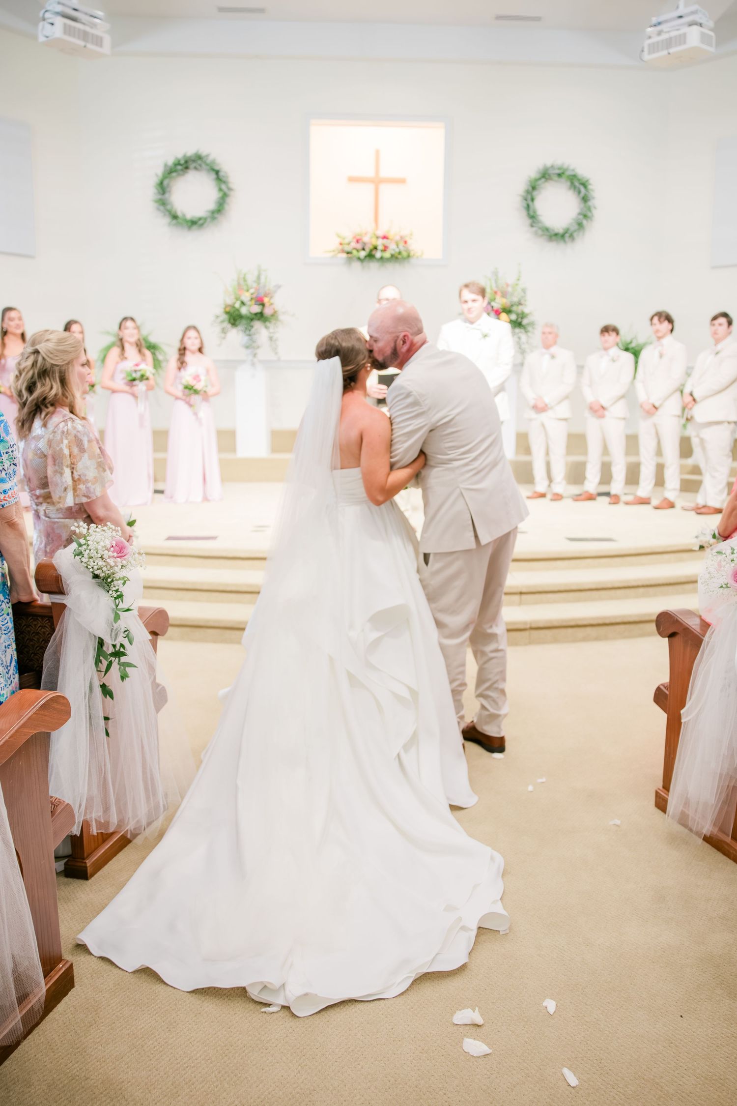 Bride and groom share their first kiss at the altar of a white church during their wedding ceremony.