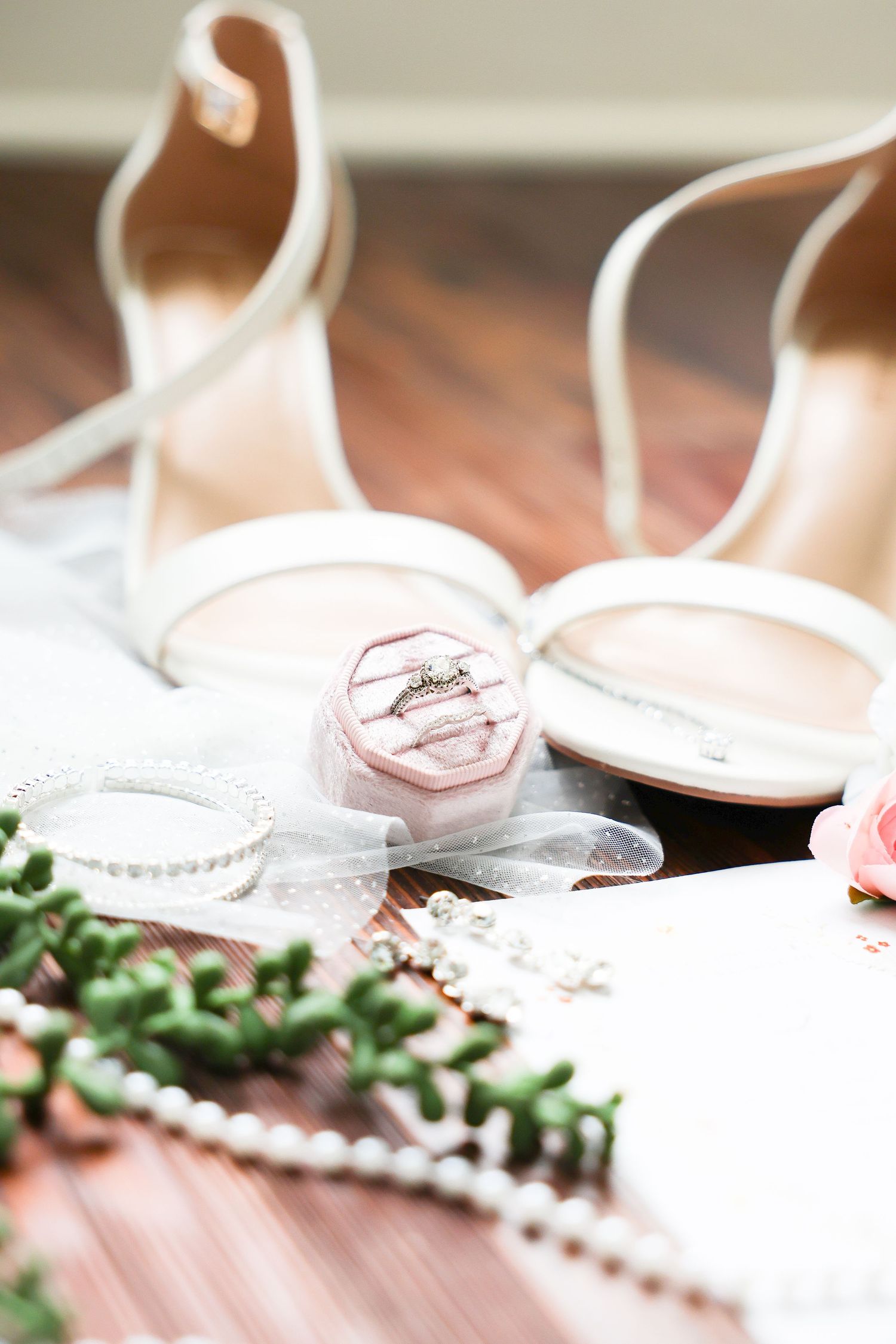 Wedding flat lay featuring diamond ring in pink velvet box, pearl jewelry, and nude strappy heels.