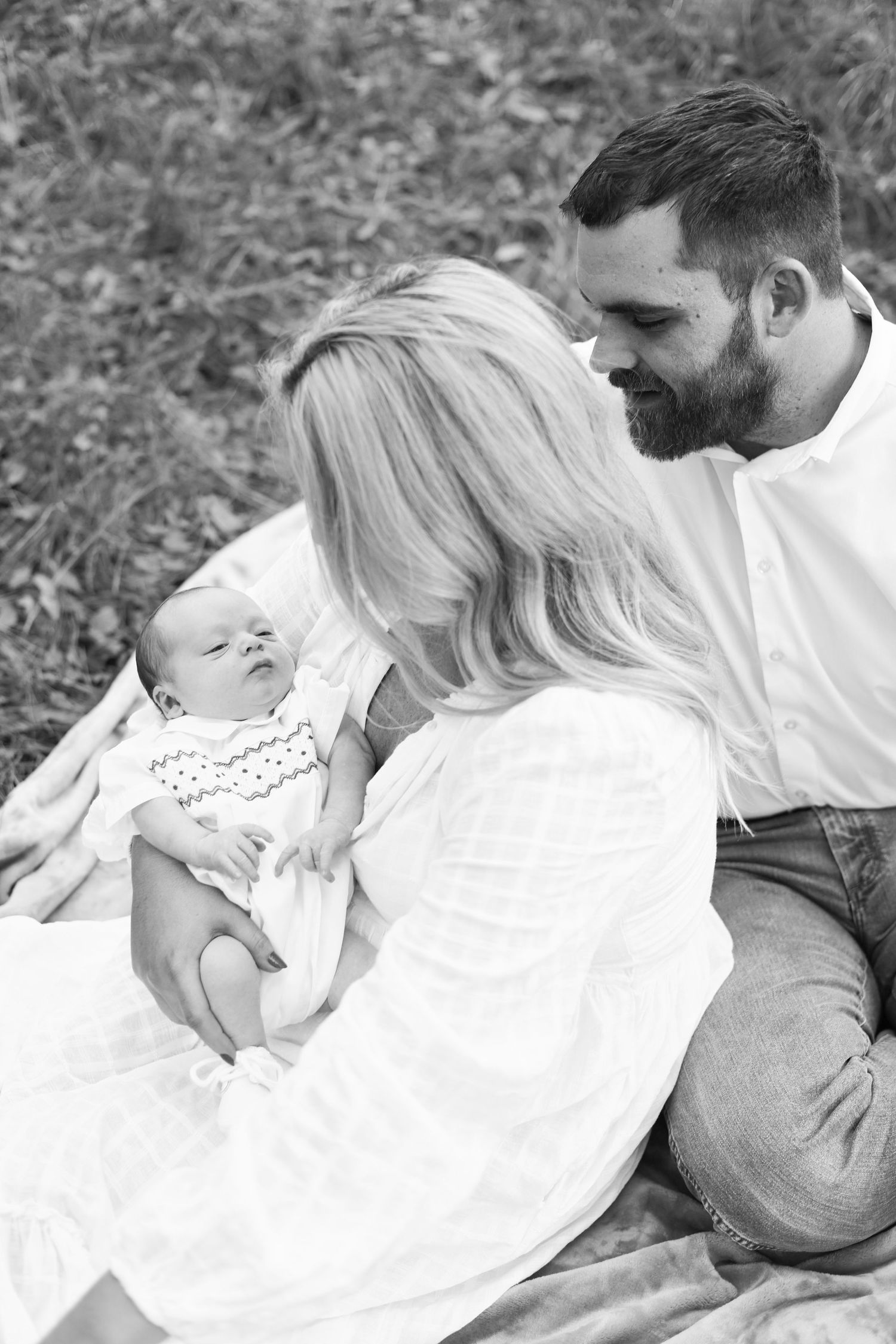 A tender black and white family moment outdoors as parents share a special moment with their newborn baby on a blanket.