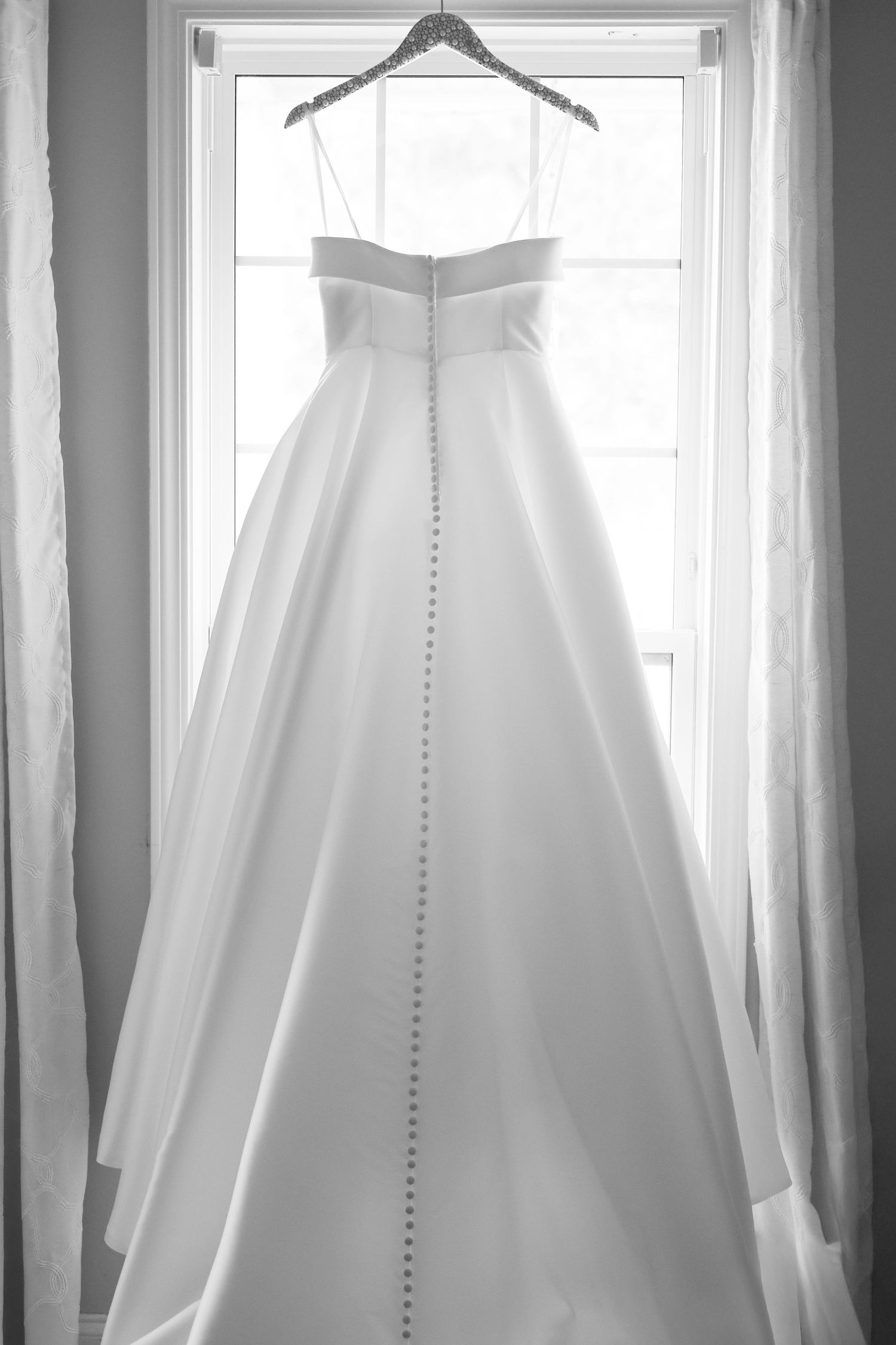 Multiple views of an elegant white wedding dress with buttons hanging in a bright window with natural light.