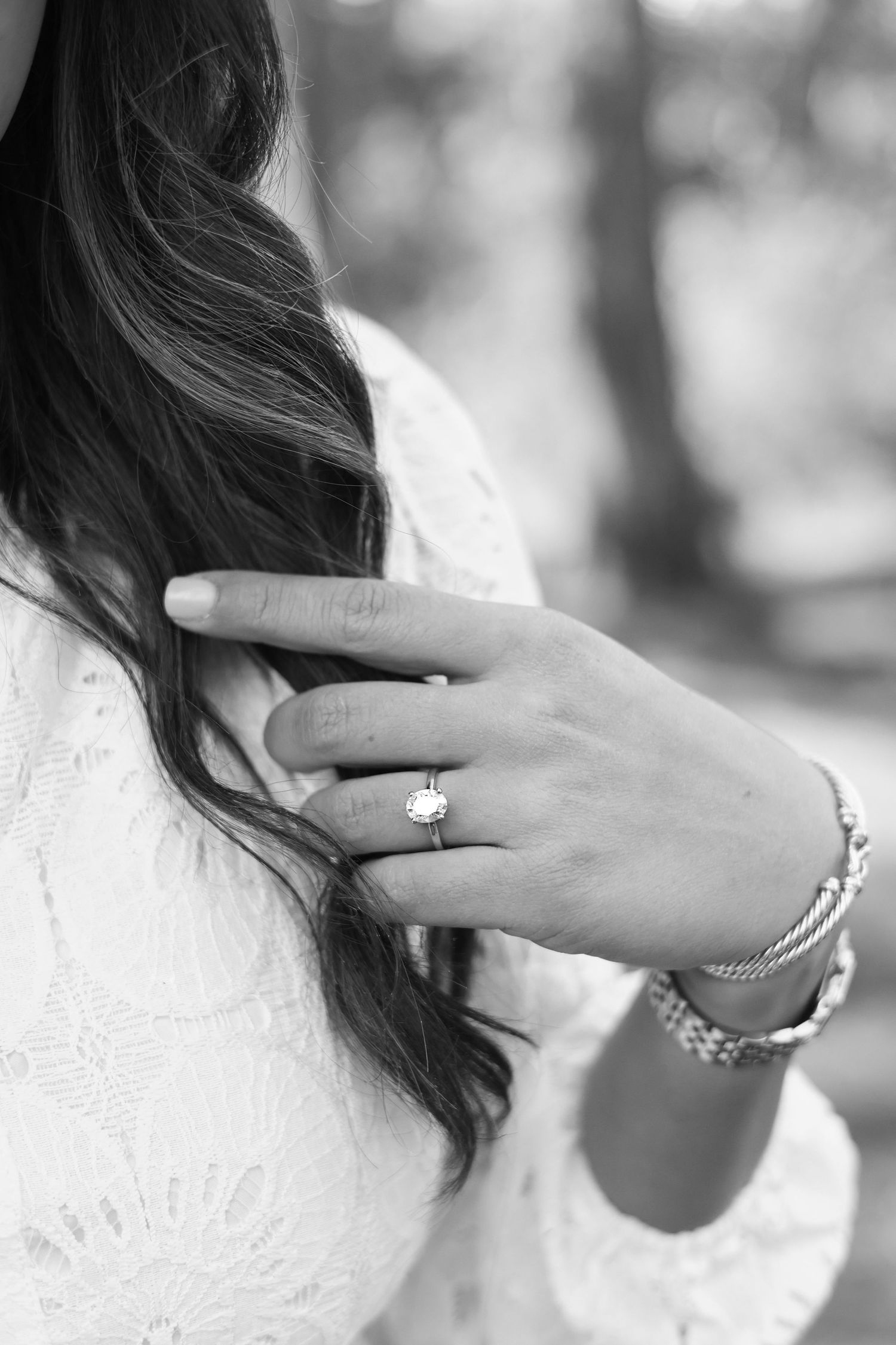 Close-up of an engagement ring being shown on a woman's hand with dark wavy hair in the background.