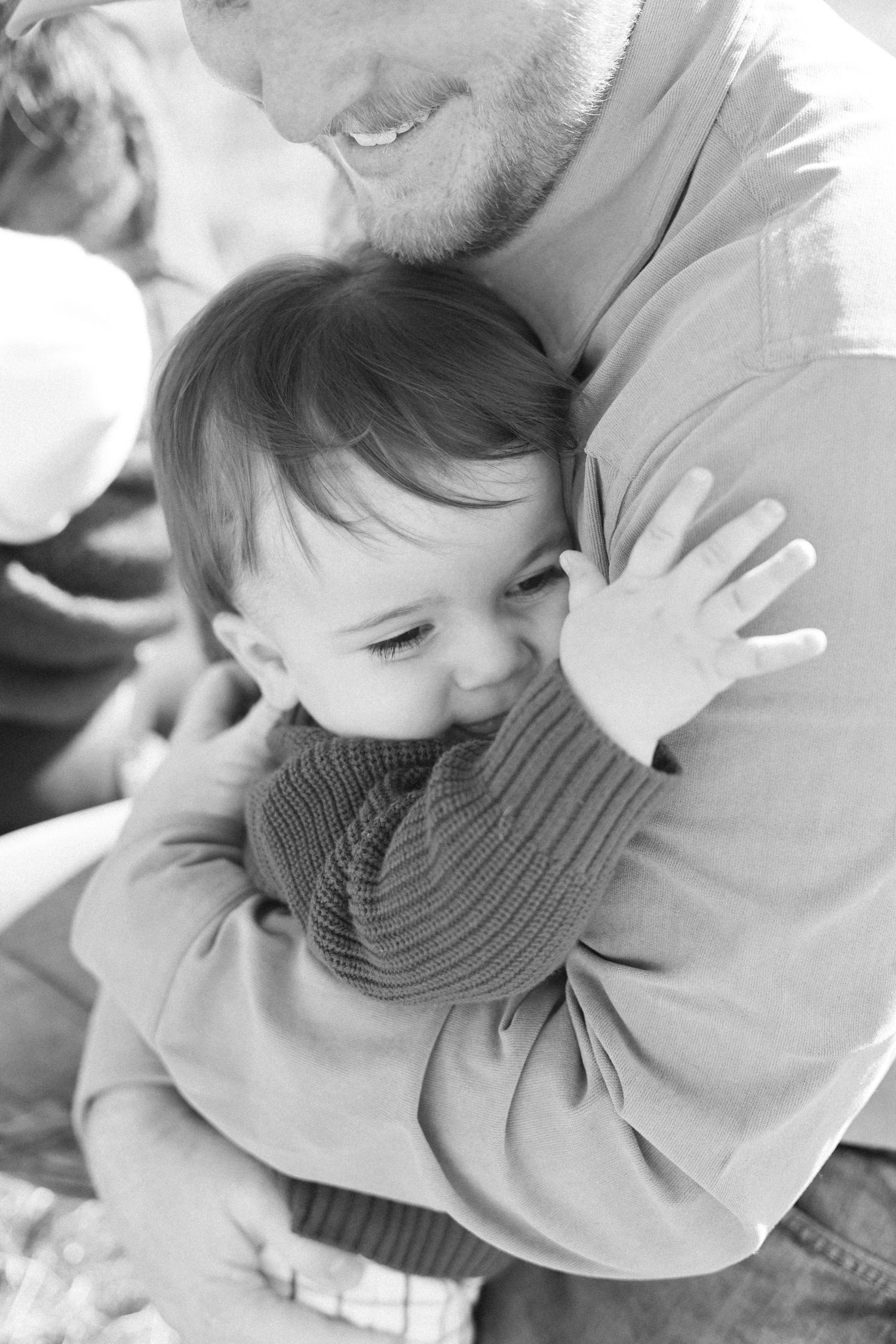 Black and white candid shots of tender family moments with a baby in a knit sweater.