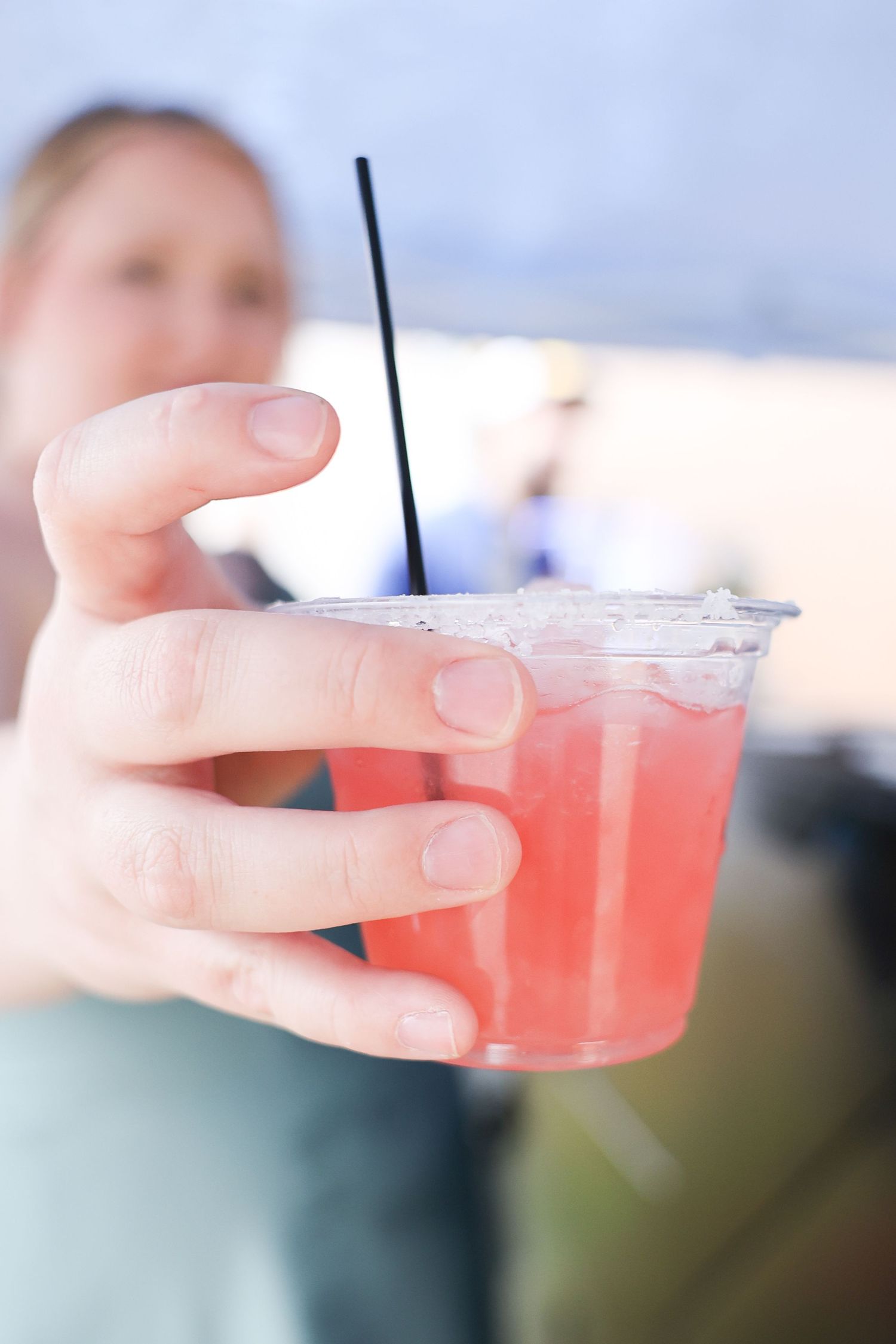 Close-up of a hand holding a pink cocktail in a plastic cup with a black straw at a wedding.