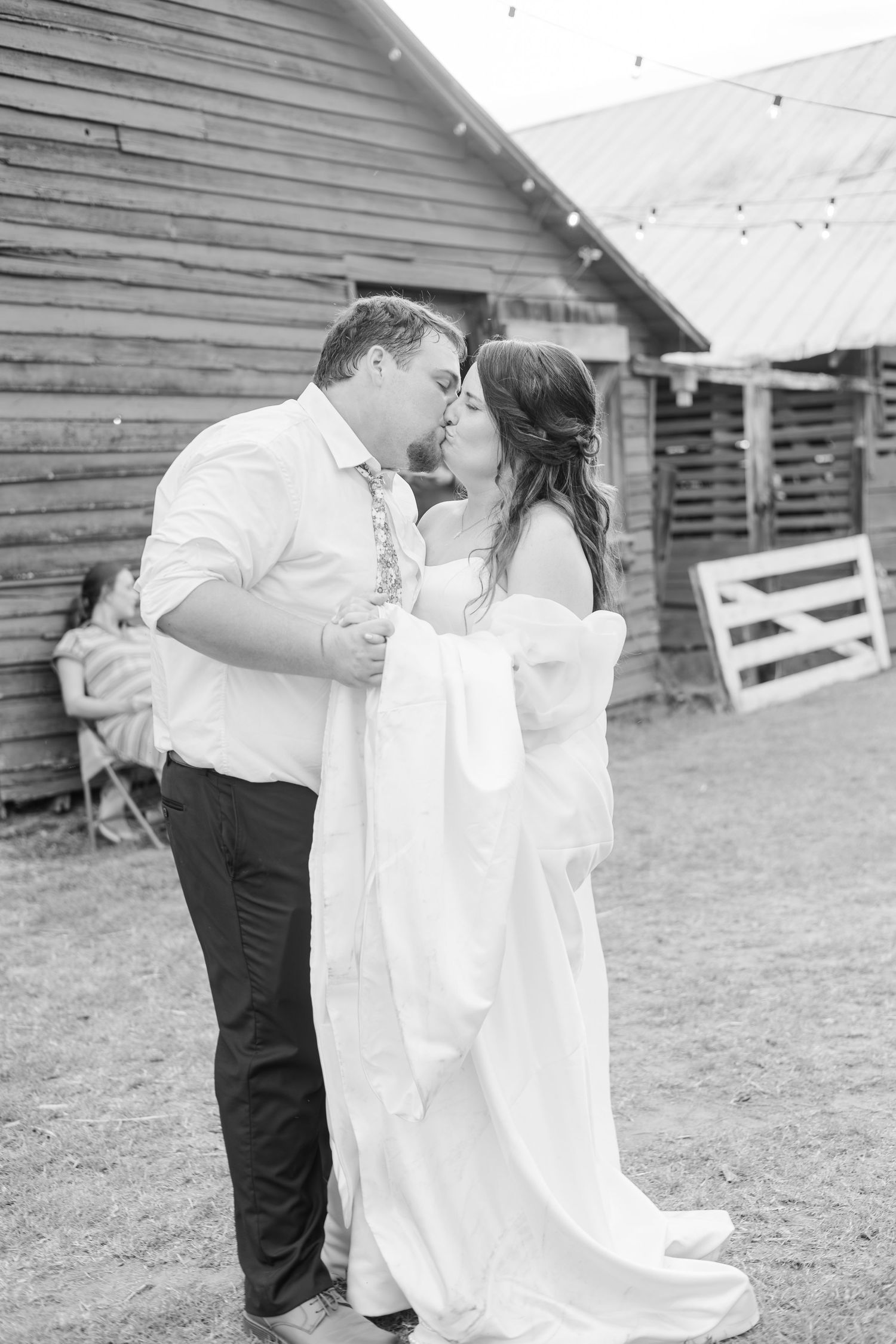 Bride and groom sharing a kiss outside a rustic barn at their wedding, black and white photo.