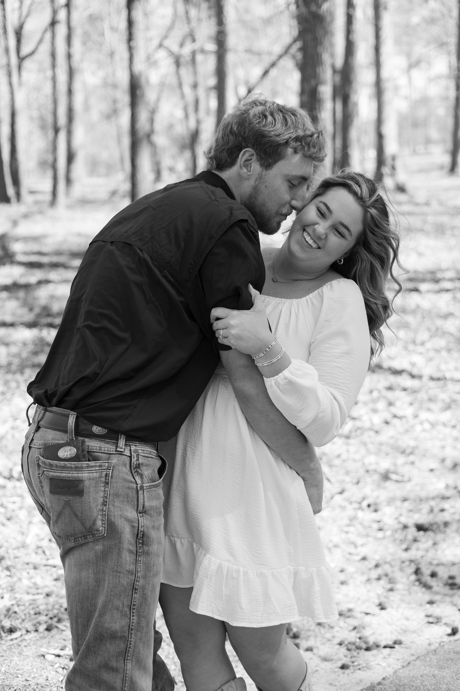 A couple shares tender romantic moments in a wooded outdoor setting in black and white photography.