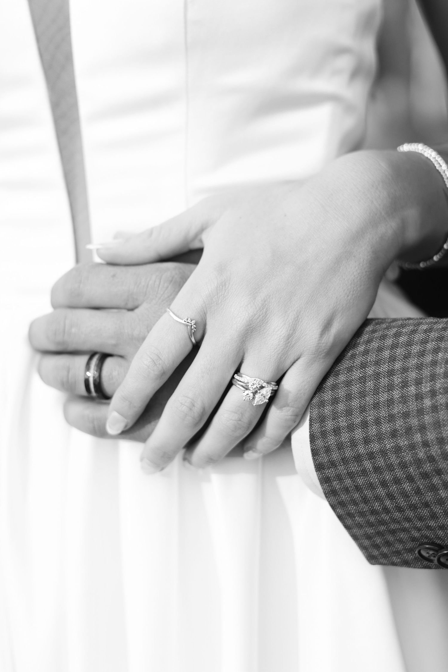 A close-up black and white photo of wedding rings and clasped hands.