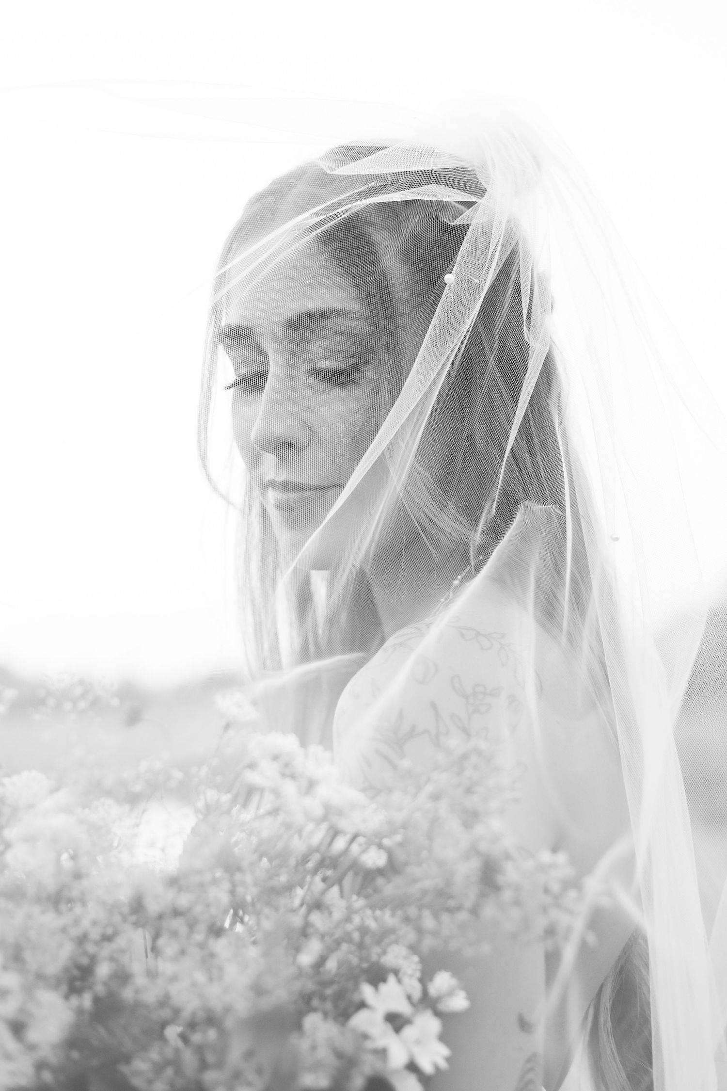 Dreamy black and white close-up of bride through delicate veil with bouquet.