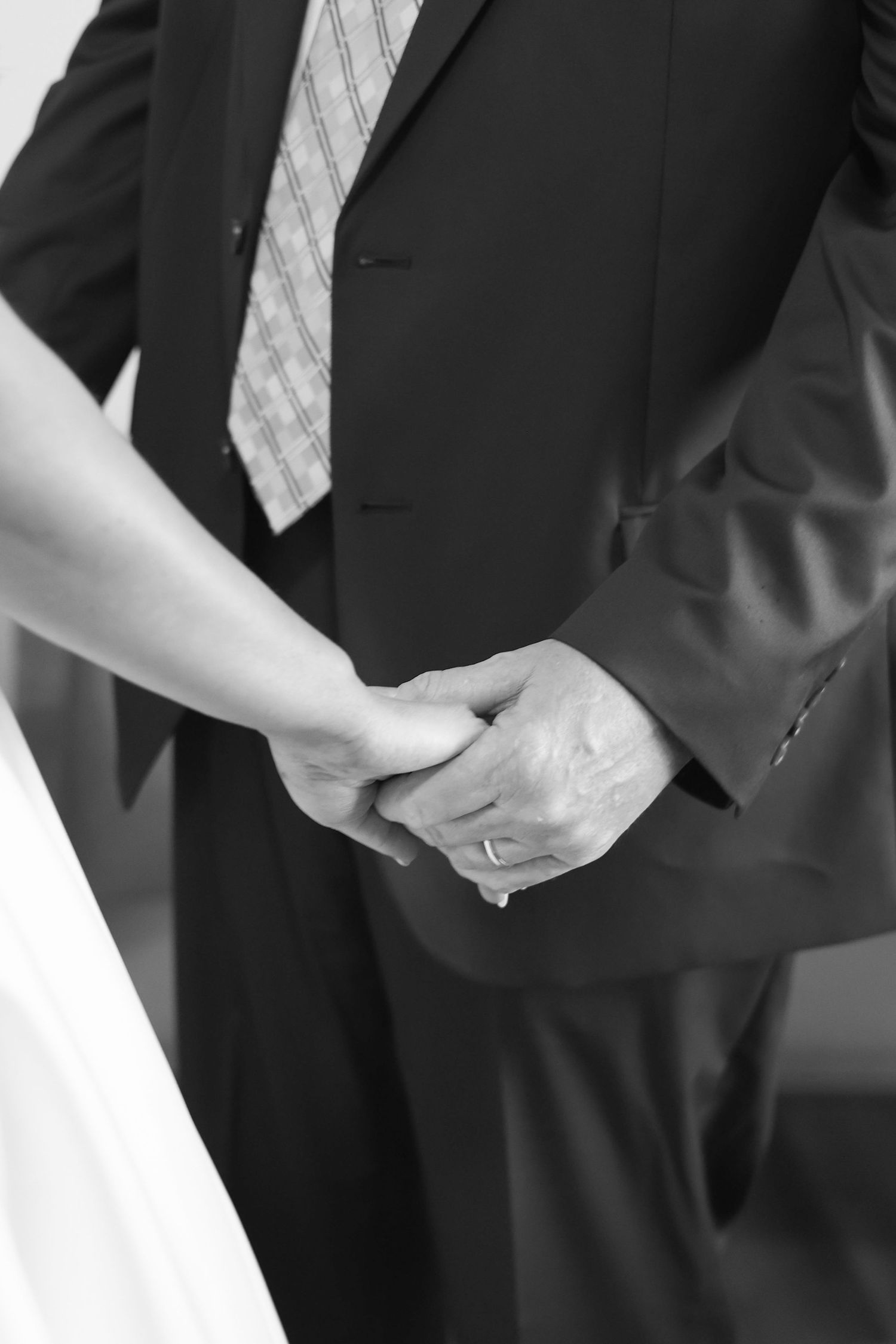 A black and white close-up photo showing hands clasped together in formal business attire.