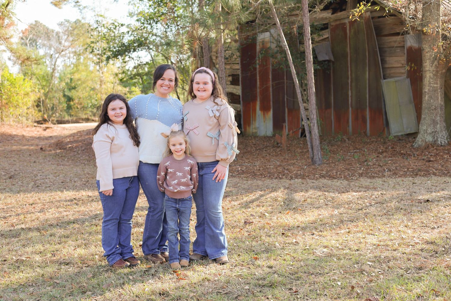 A family group poses together outdoors in coordinated casual outfits with a wooded background.