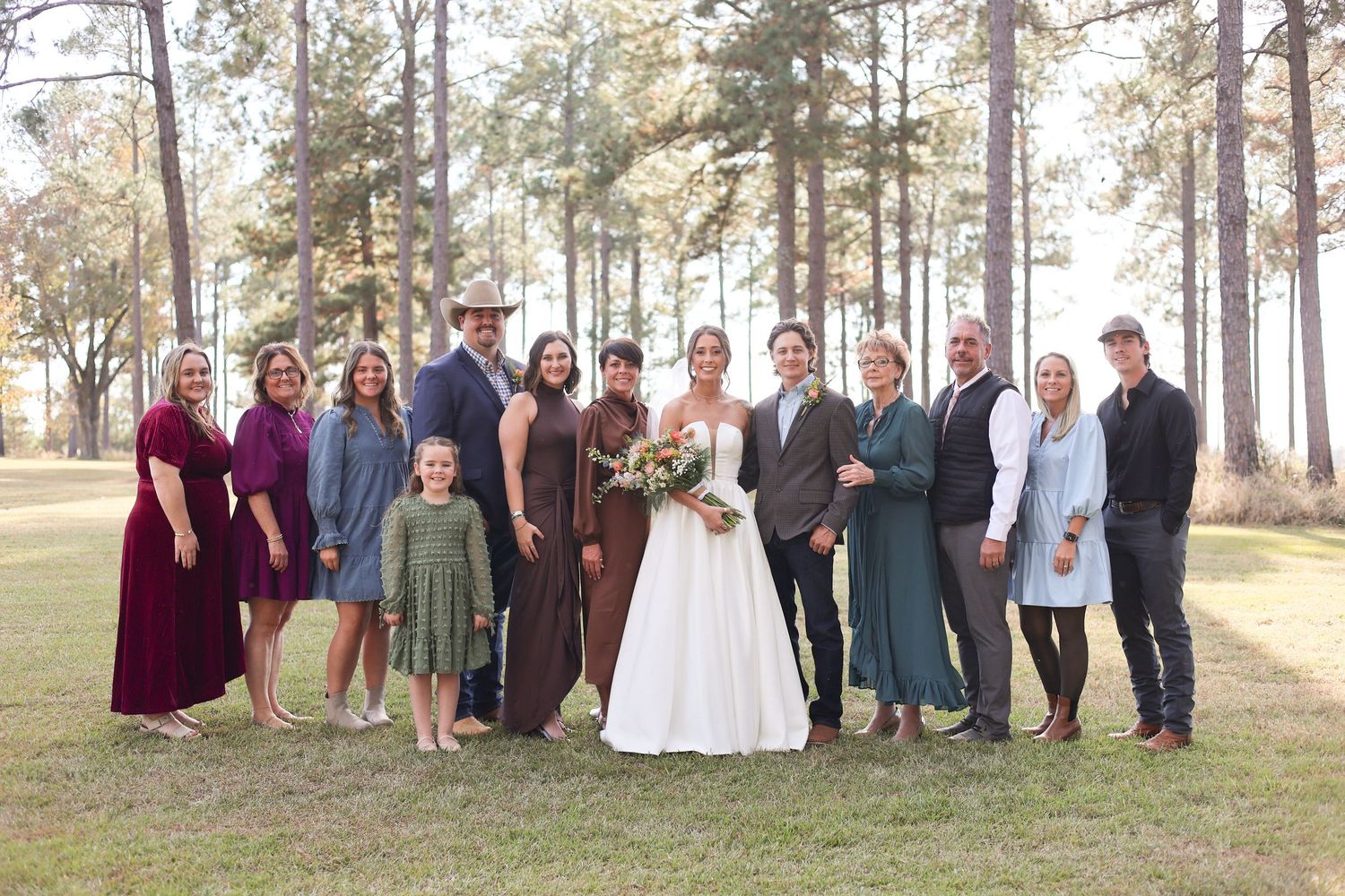 Wide group portrait of wedding guests and family members in pine forest.