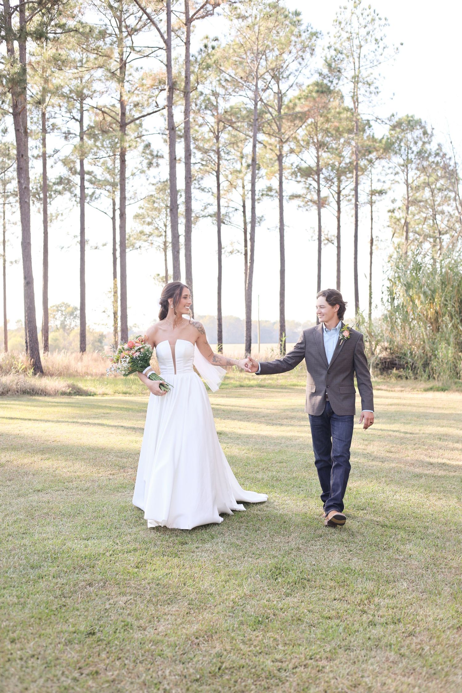 A wedding couple dances playfully in a sun-lit pine forest setting during their outdoor photo session.