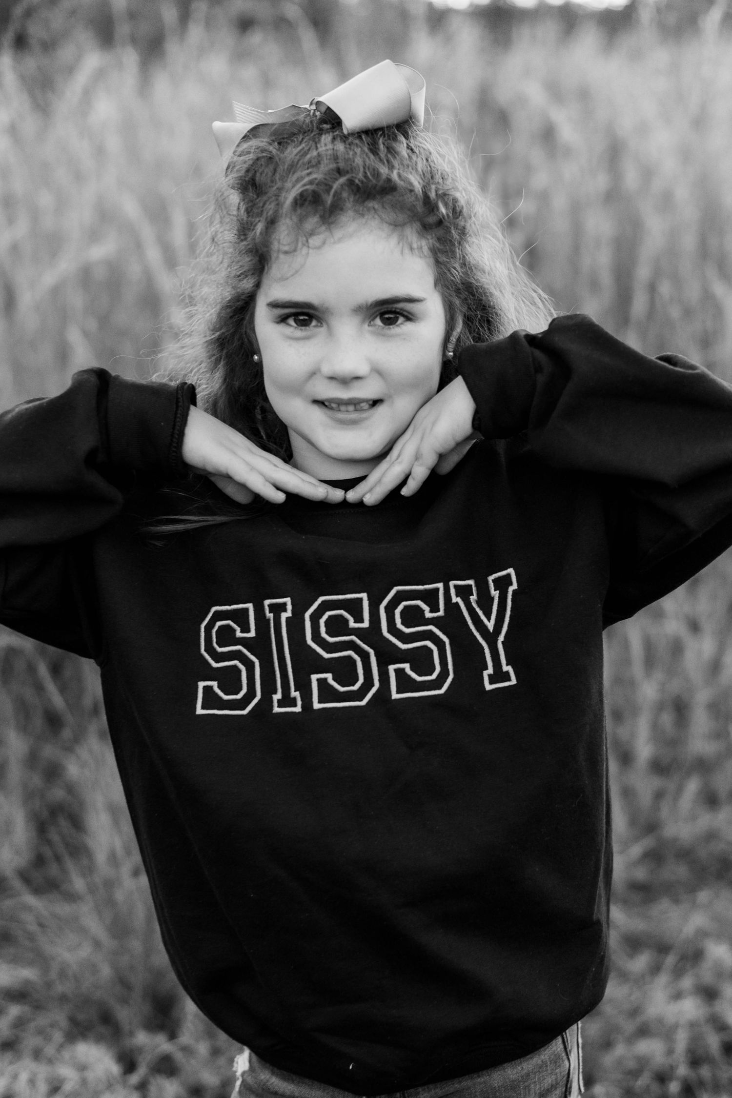 Girl in black SISSY sweatshirt poses outdoors in black and white photo with hair bow.