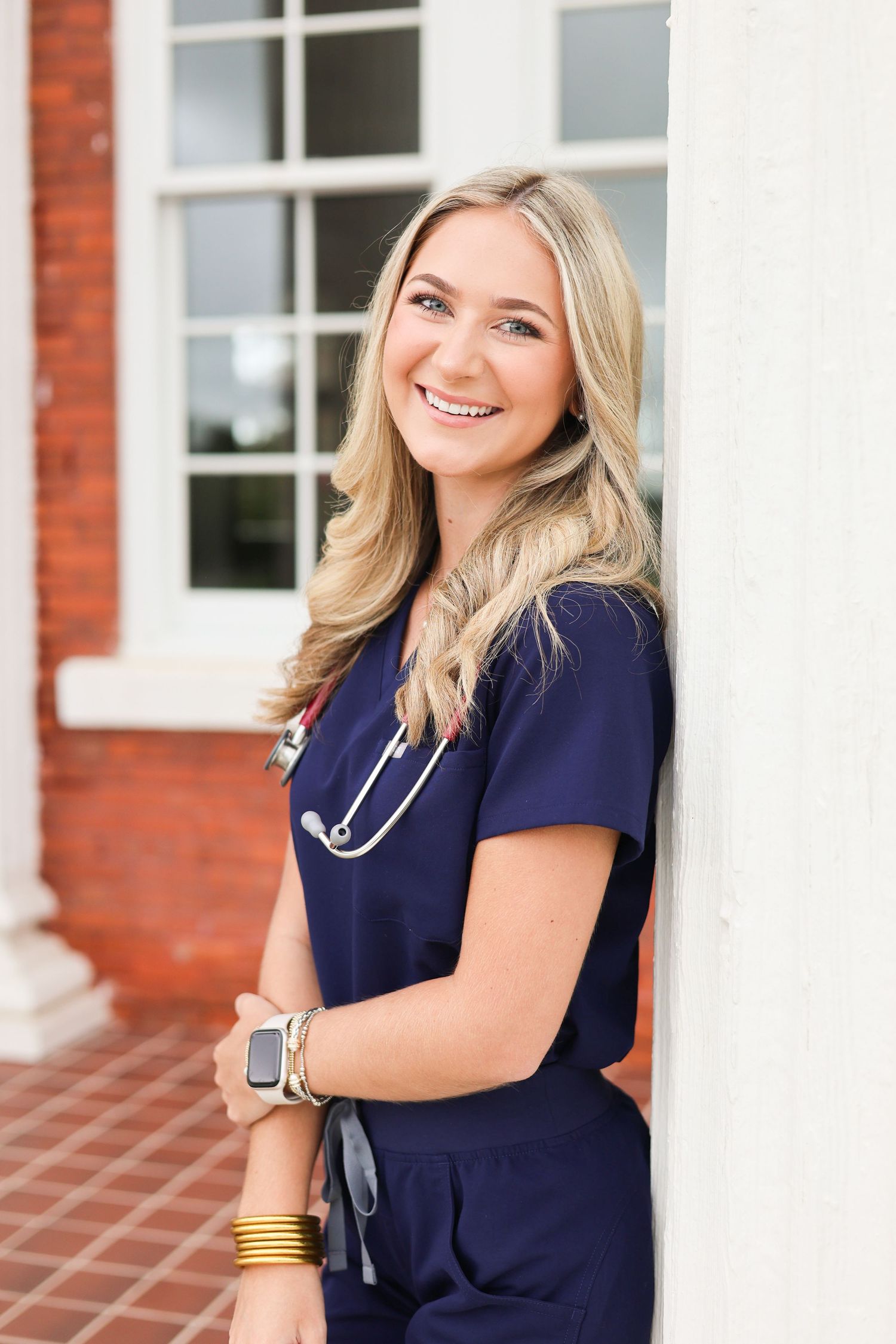 Healthcare worker in navy scrubs smiles warmly while posing against white columns.