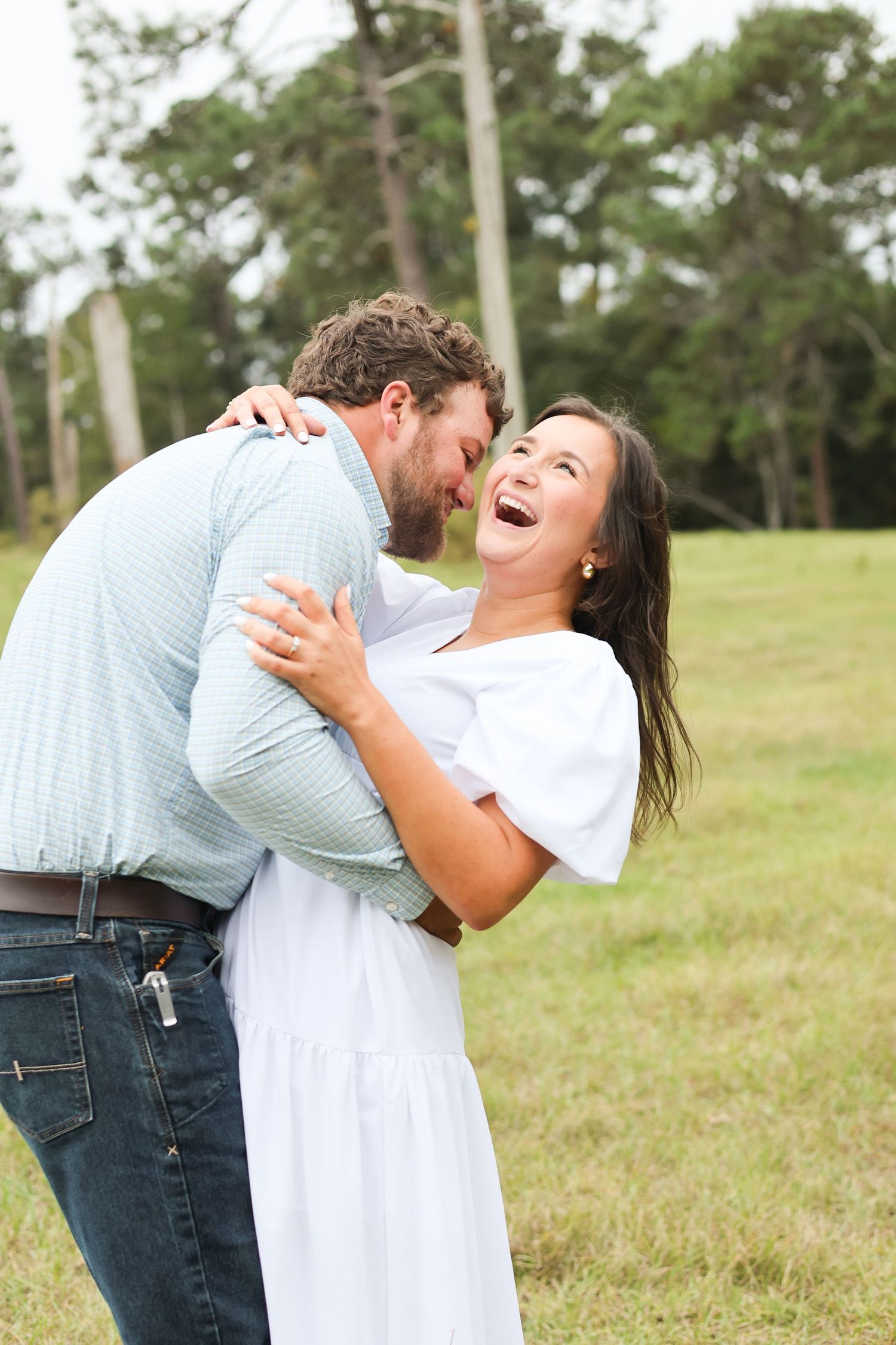 A couple shares a joyful embrace while laughing together in a grassy outdoor field.