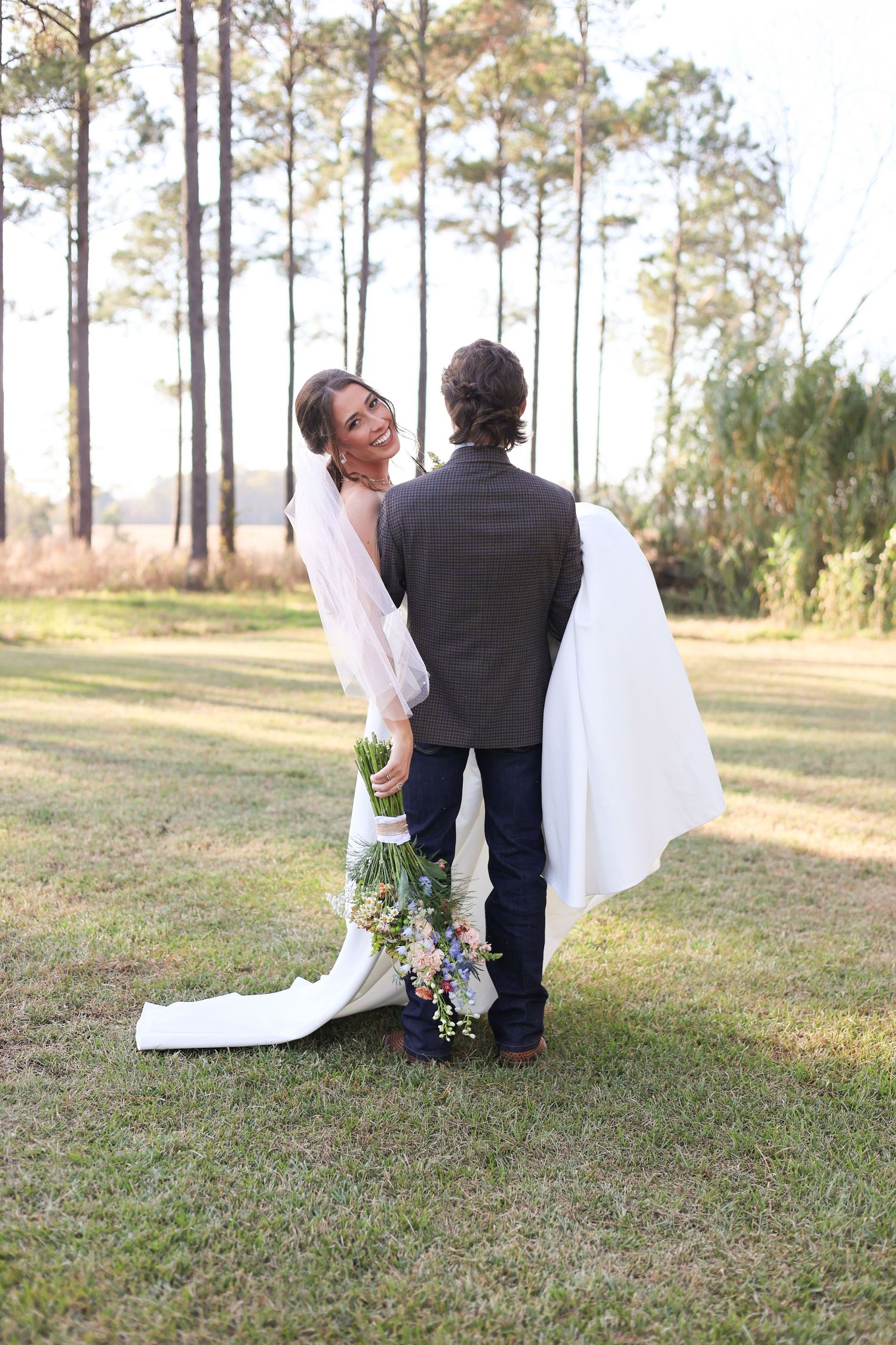A wedding couple poses with a colorful bouquet in a serene forest setting.